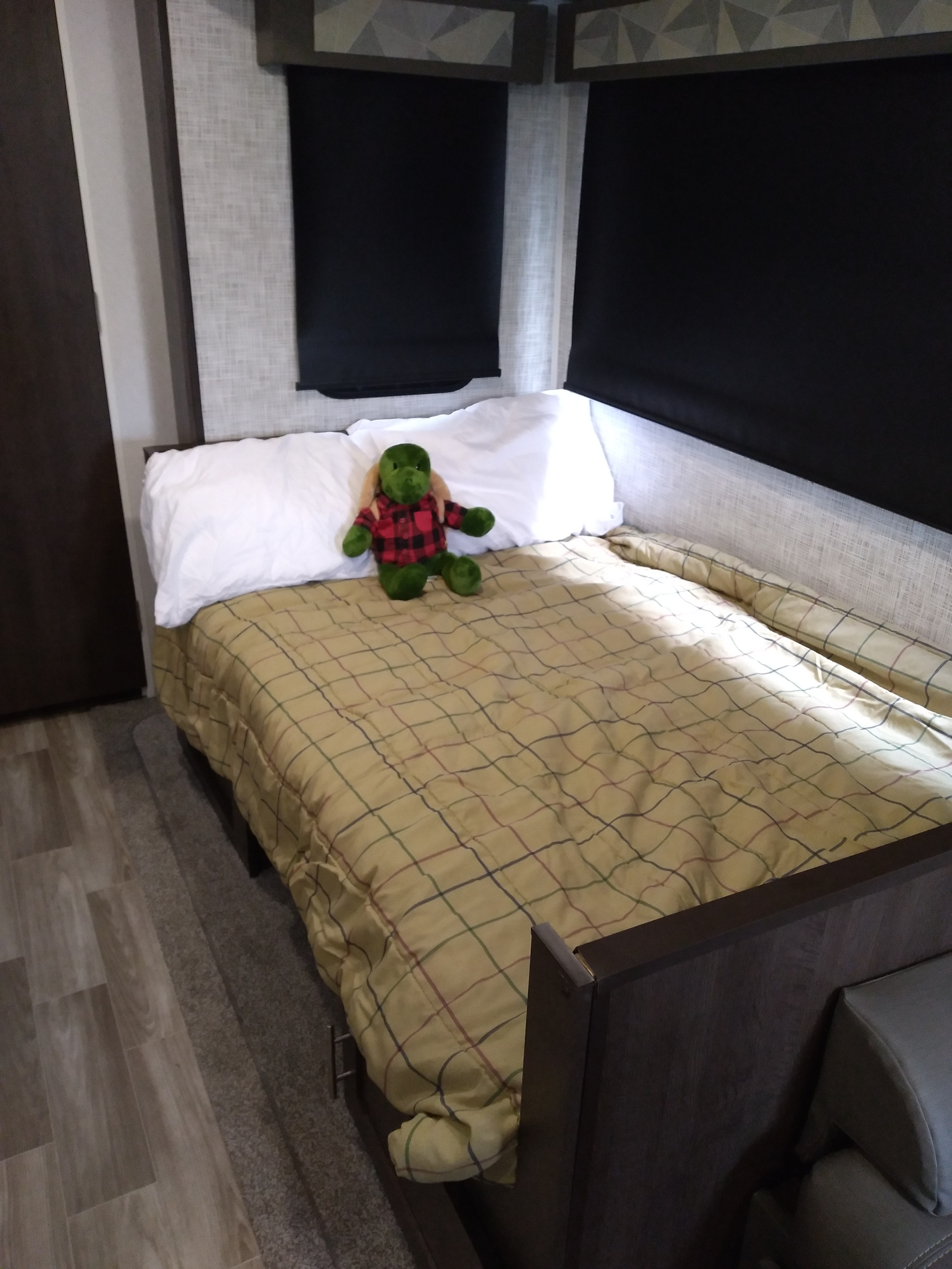 This cozy RV rental bedroom features a plaid comforter and a green stuffed animal on the bed, with pulled shades.. Forest River Other 2020