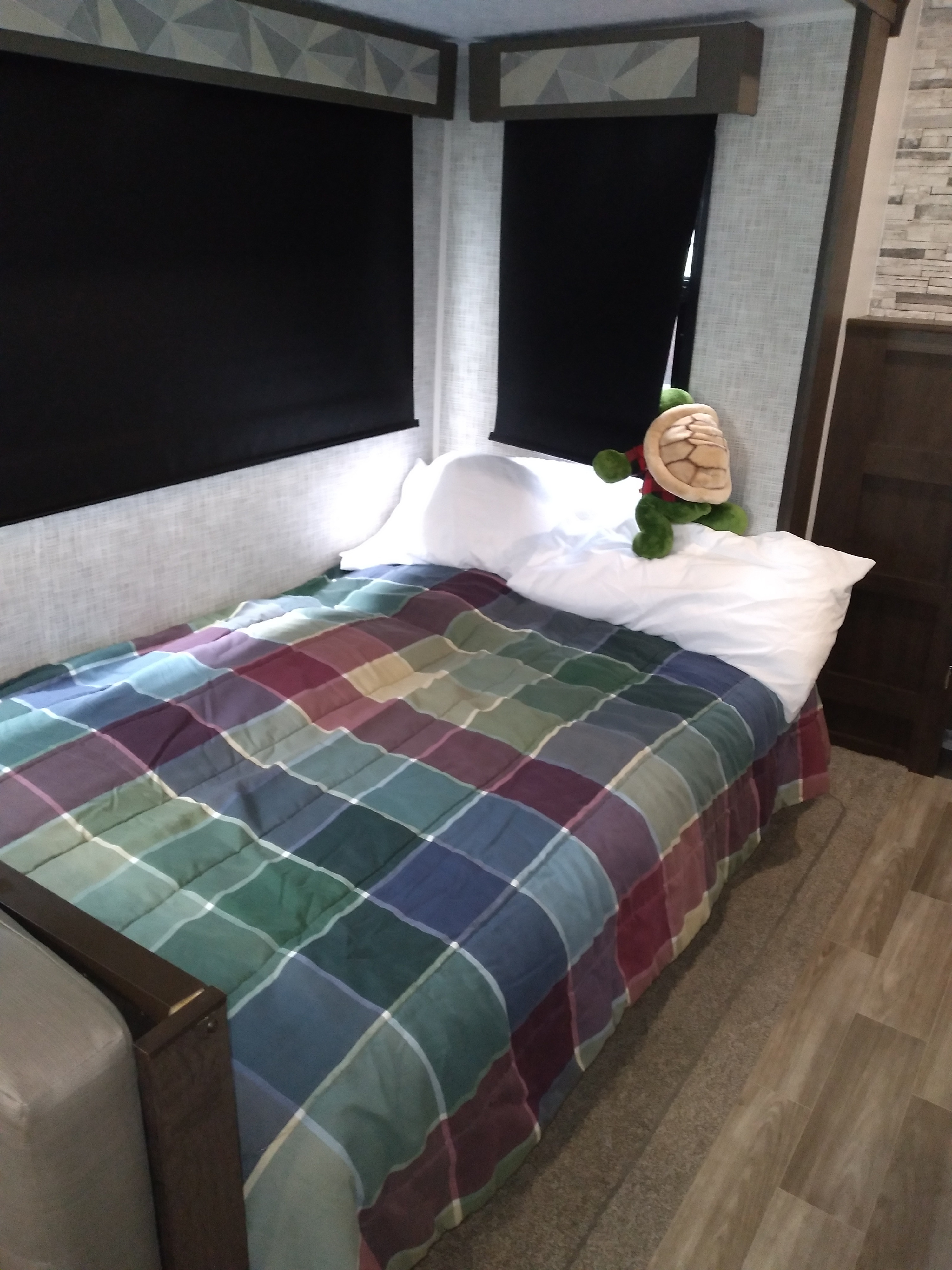 Inside an RV rental: a cozy bedroom with a colorful plaid comforter, white pillows, and a turtle toy.. Forest River Other 2020