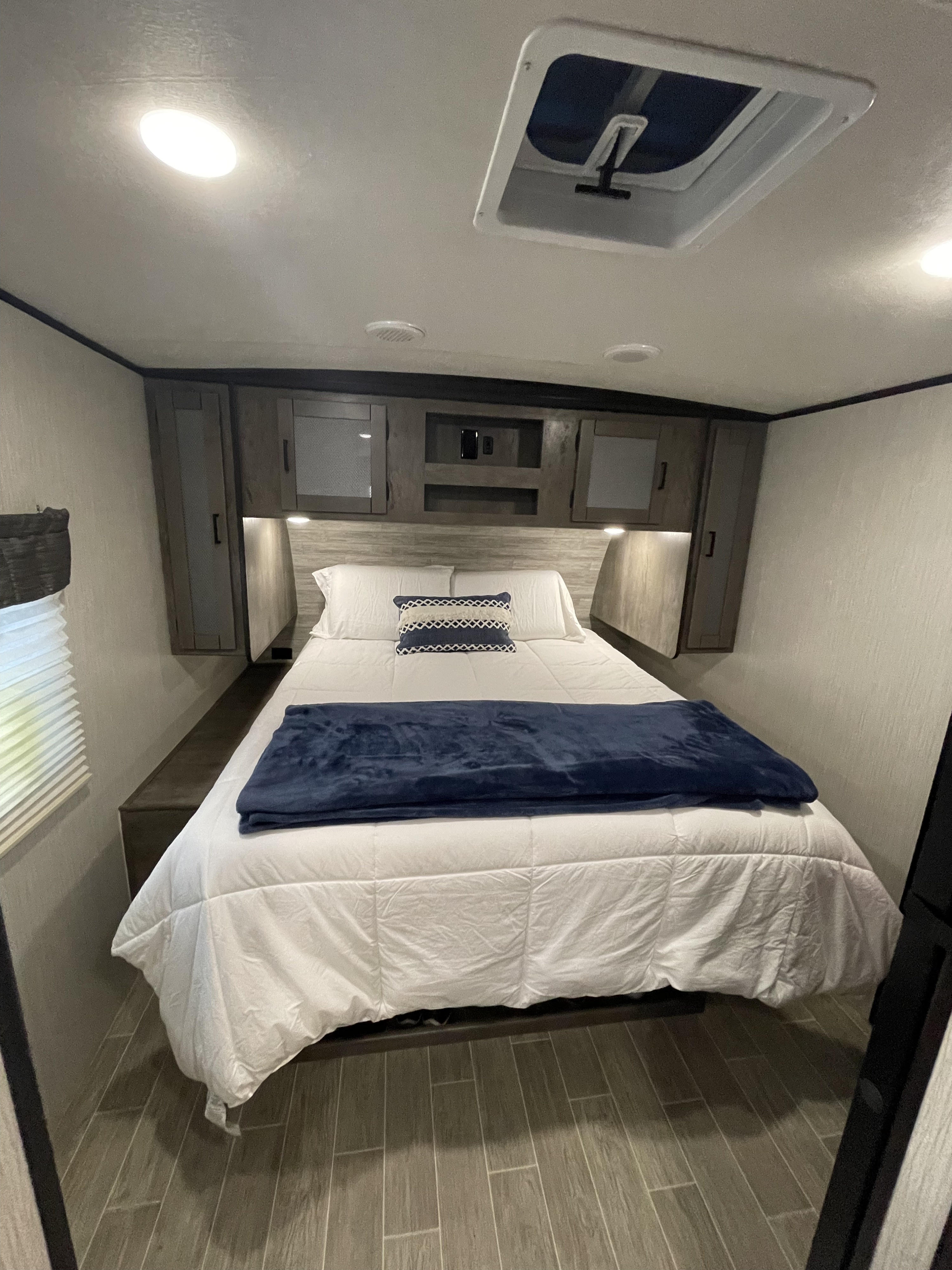 Inside a cozy RV rental: a bright bedroom features a queen bed with white bedding, blue accents, and built-in storage.. Heartland RVs Wilderness 2020