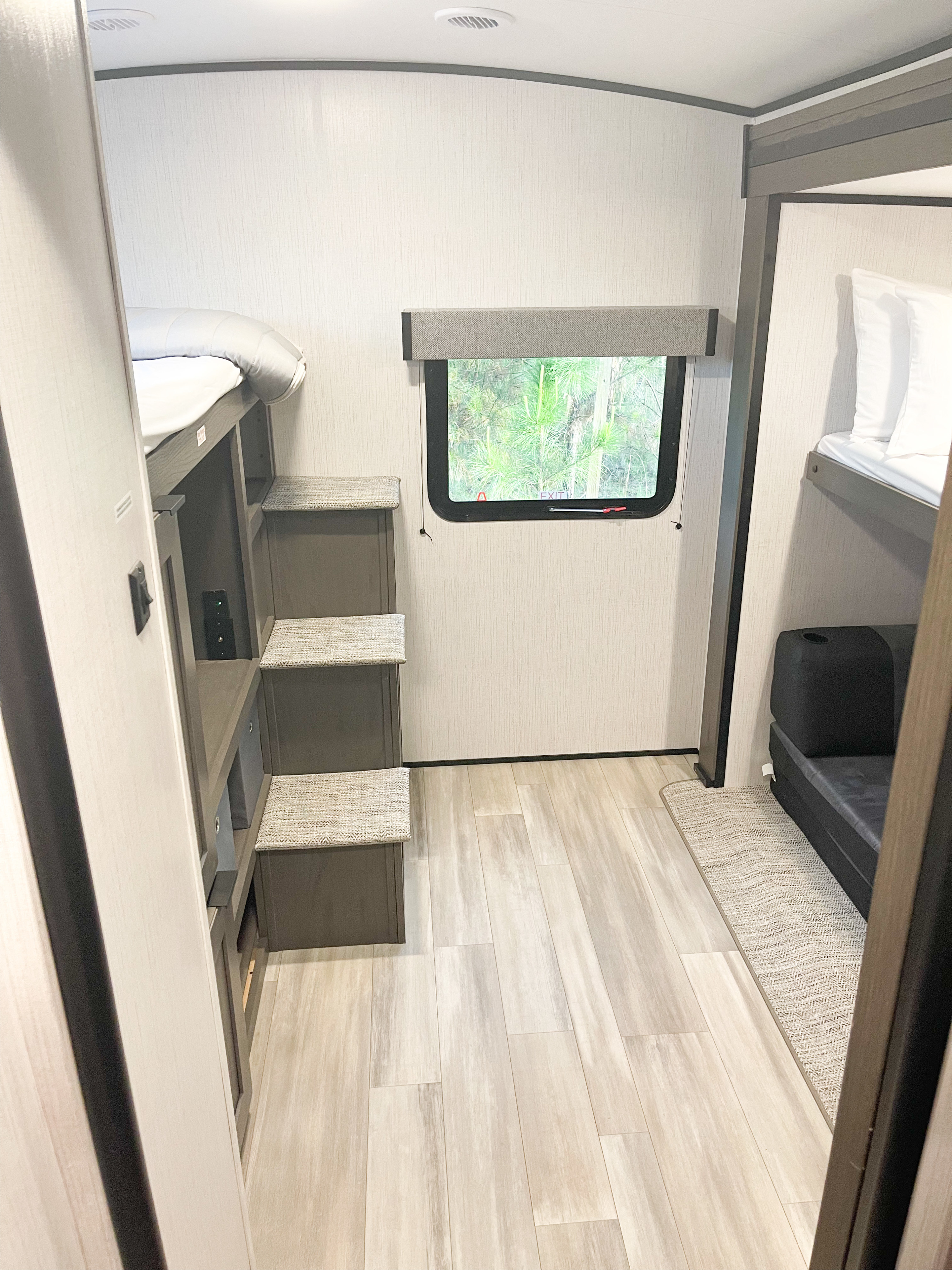 RV rental bunk room showing integrated steps, a window with a treeline view, and a small convertible couch/bed. Light, modern interior.. Cruiser RV MGP 3100BH 2022