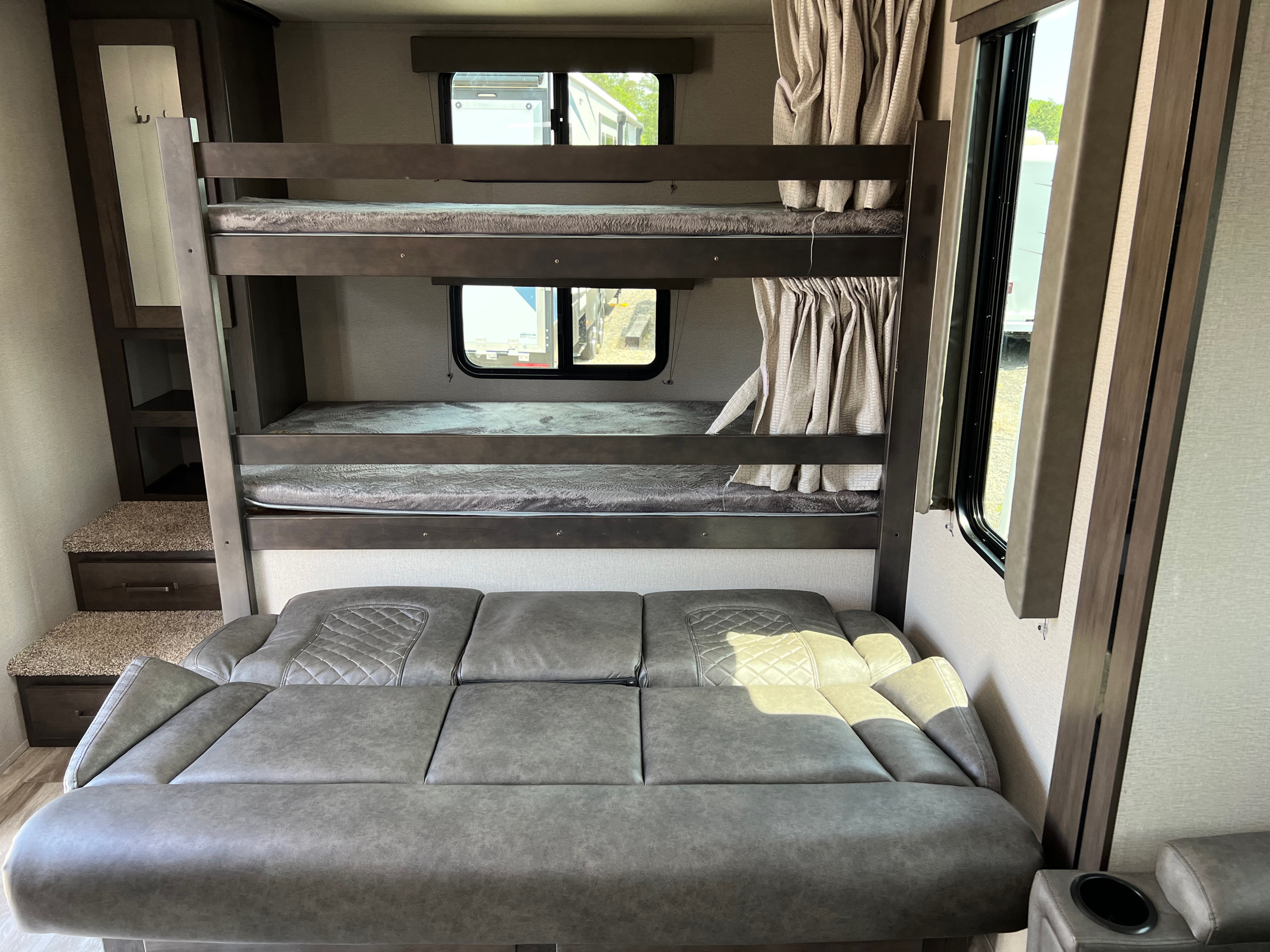 RV rental interior: cozy bunk beds with soft mattresses, a gray sofa, and built-in storage steps for comfort.. Grand Design Transcend 265BH 2022