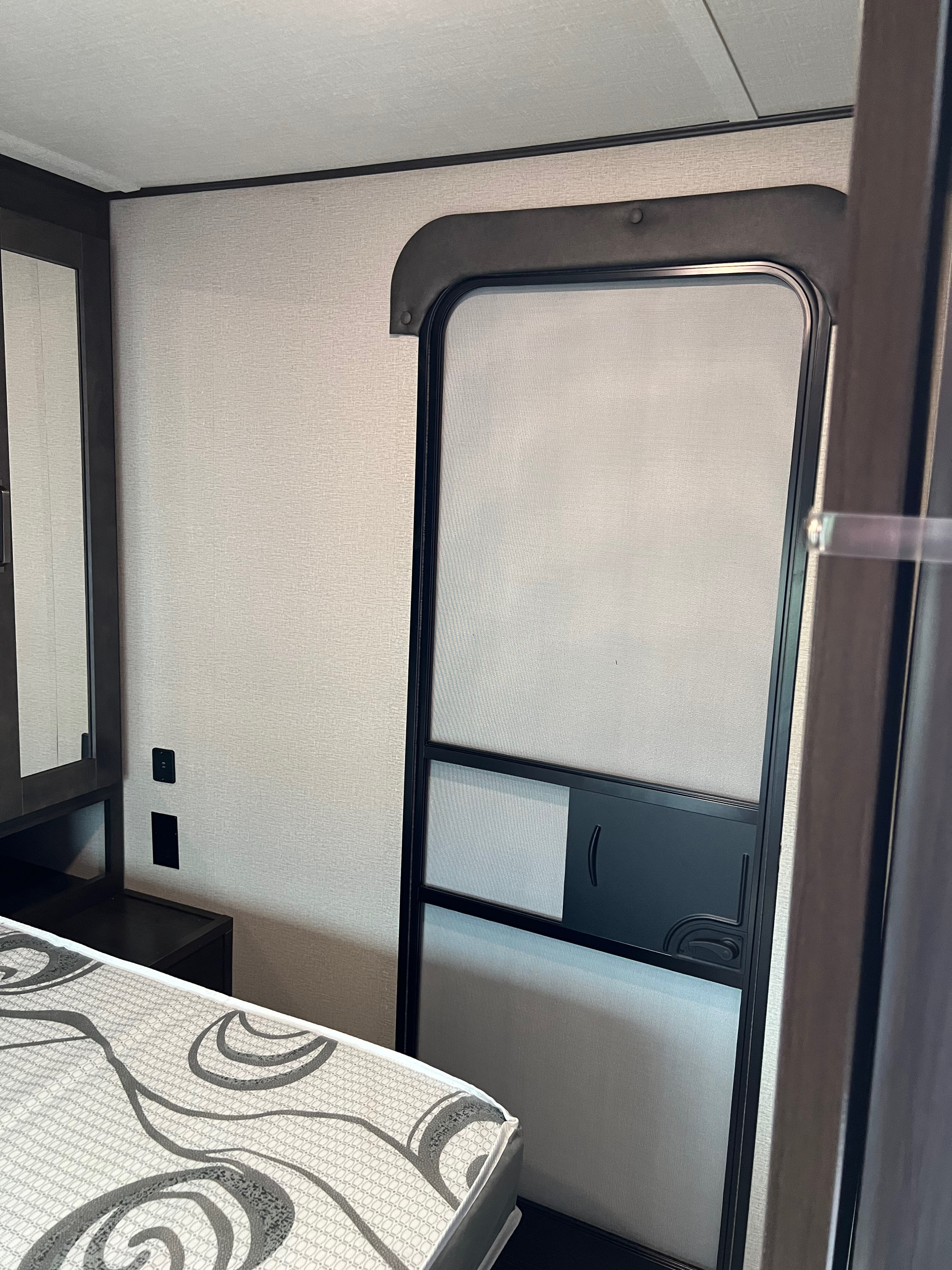 RV rental bedroom: showing a screen door, patterned mattress, and wall outlets in a compact, functional space.. Grand Design Transcend 265BH 2022