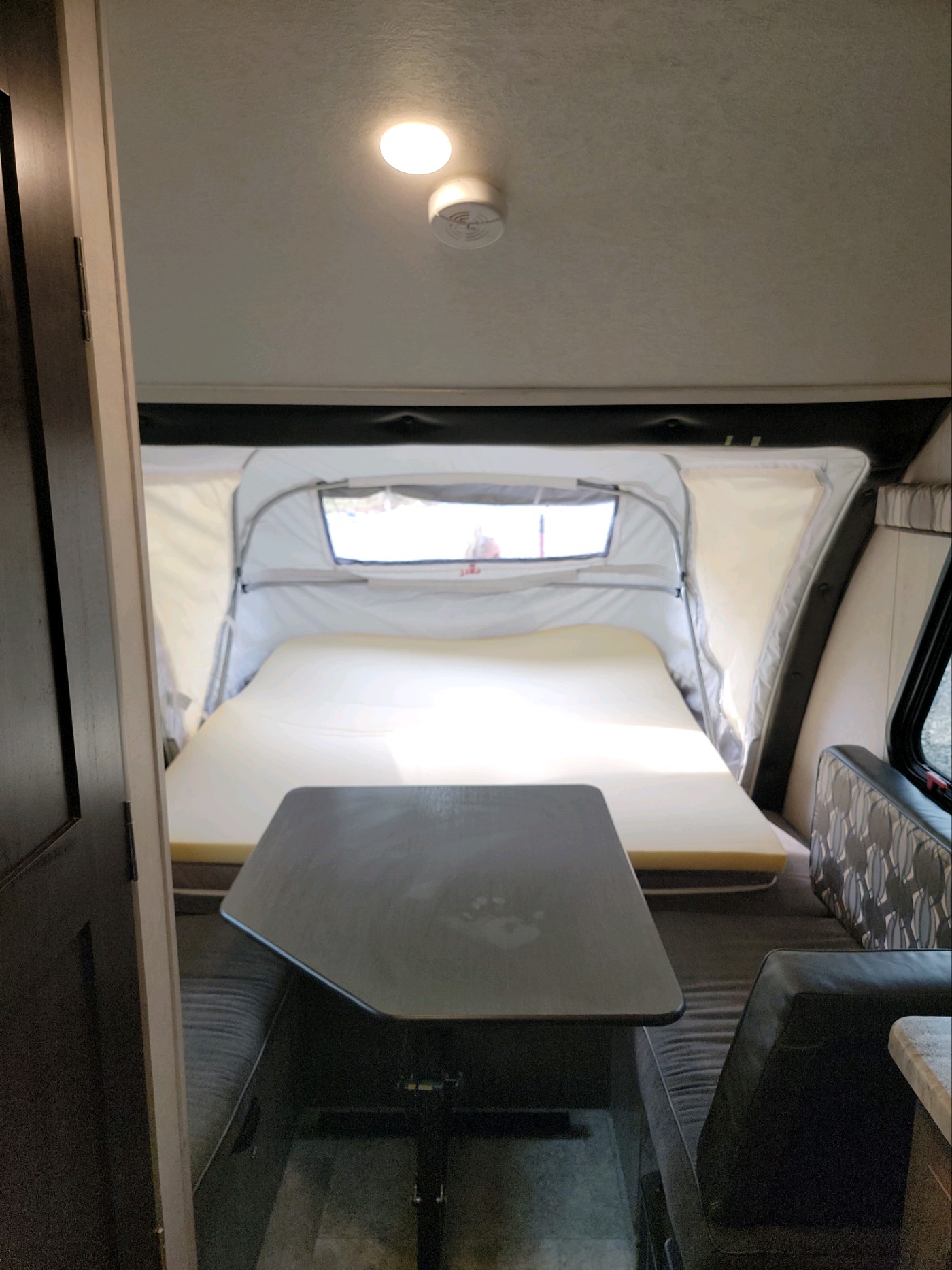 Inside this rv rental: a comfy pop-out sleeping area with mattress, dining table, benches, ceiling light, and smoke detector.. Forest River RP-176T 2018