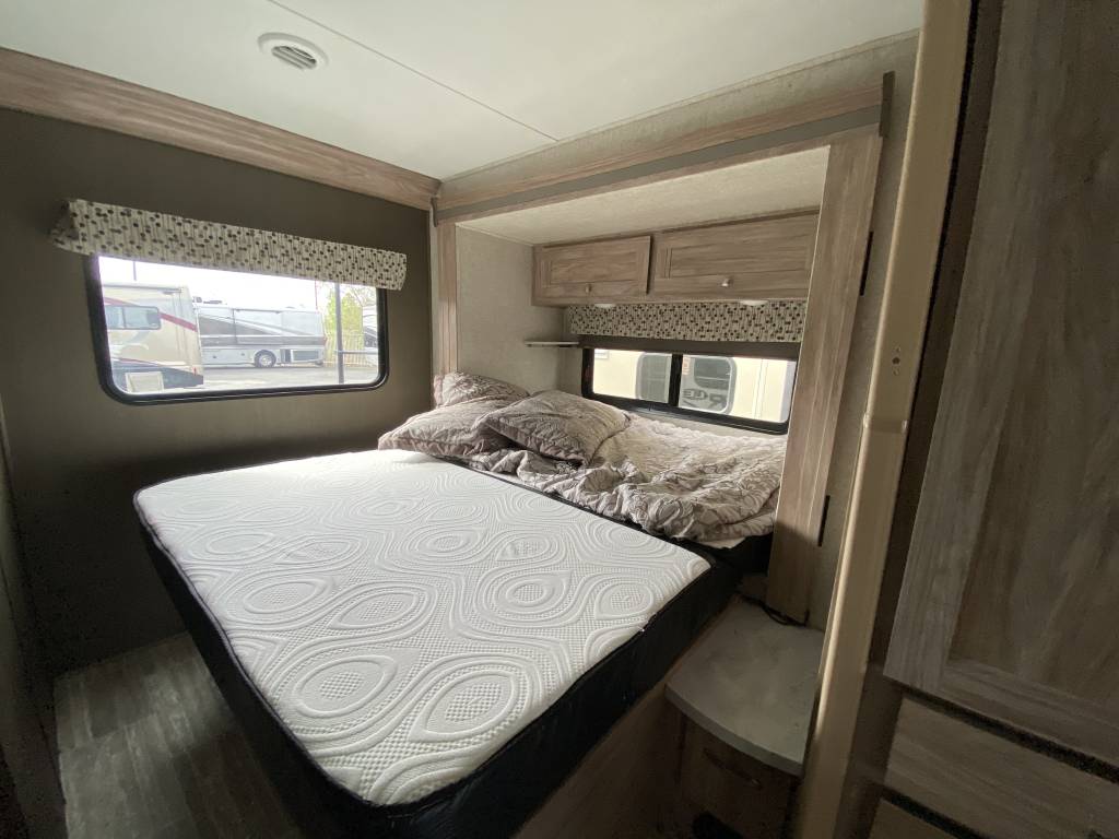Explore a cozy RV rental bedroom. It features a bed with white mattress, patterned bedding, window, and storage cabinets.. Forest River Sunseeker LE 2020