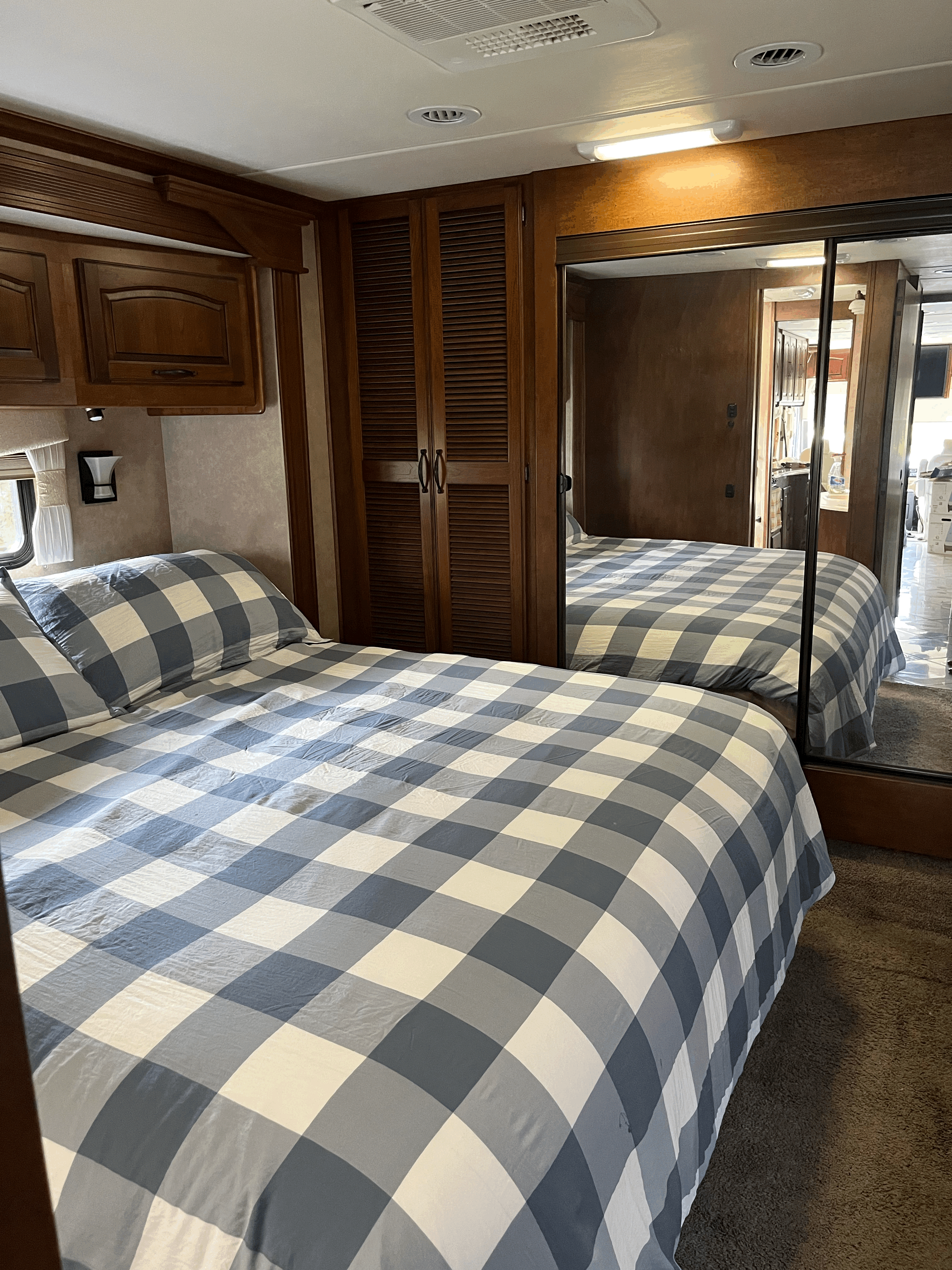 Cozy RV rental bedroom with blue plaid bedding, wood cabinetry, and large mirror reflecting the space, offering a comfortable stay.. Forest River Coachmen Cross Country 2013