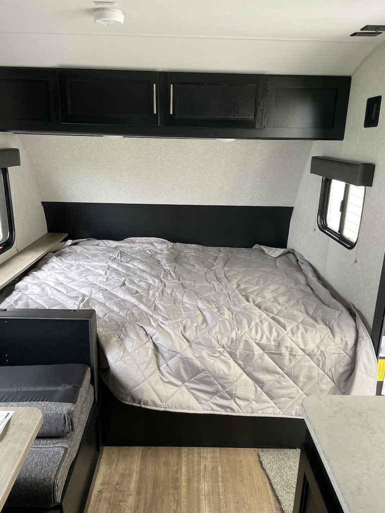 Spacious RV rental bedroom with a large, comfortable bed, overhead black cabinets, and side windows.. Forest River Cherokee Wolf Pup 2022