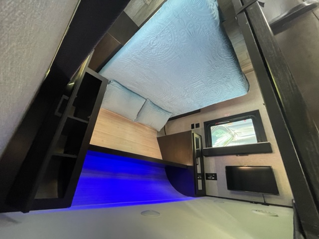 This RV rental features a comfortable bed, lighted desk with shelves, and a wall-mounted TV in a compact living space.. Jayco 267 BHS F 2022