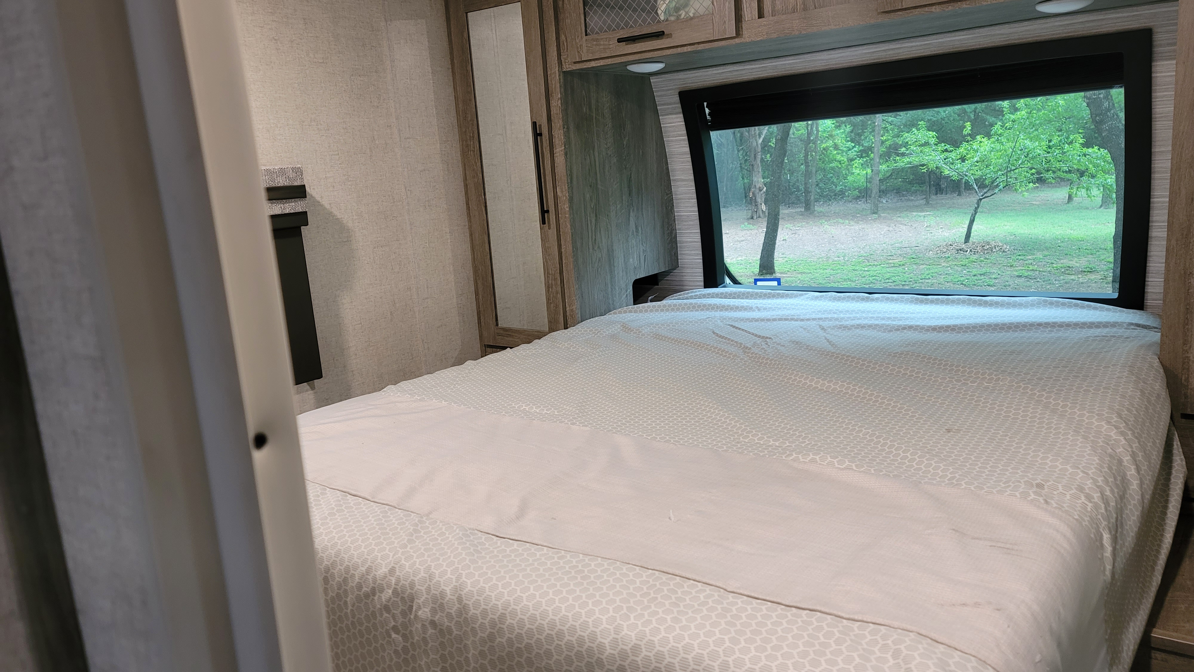 Cozy RV rental bedroom with a large window offering a serene nature view.. Forrest River Heritage Glen Delivery only Wildwood 2021