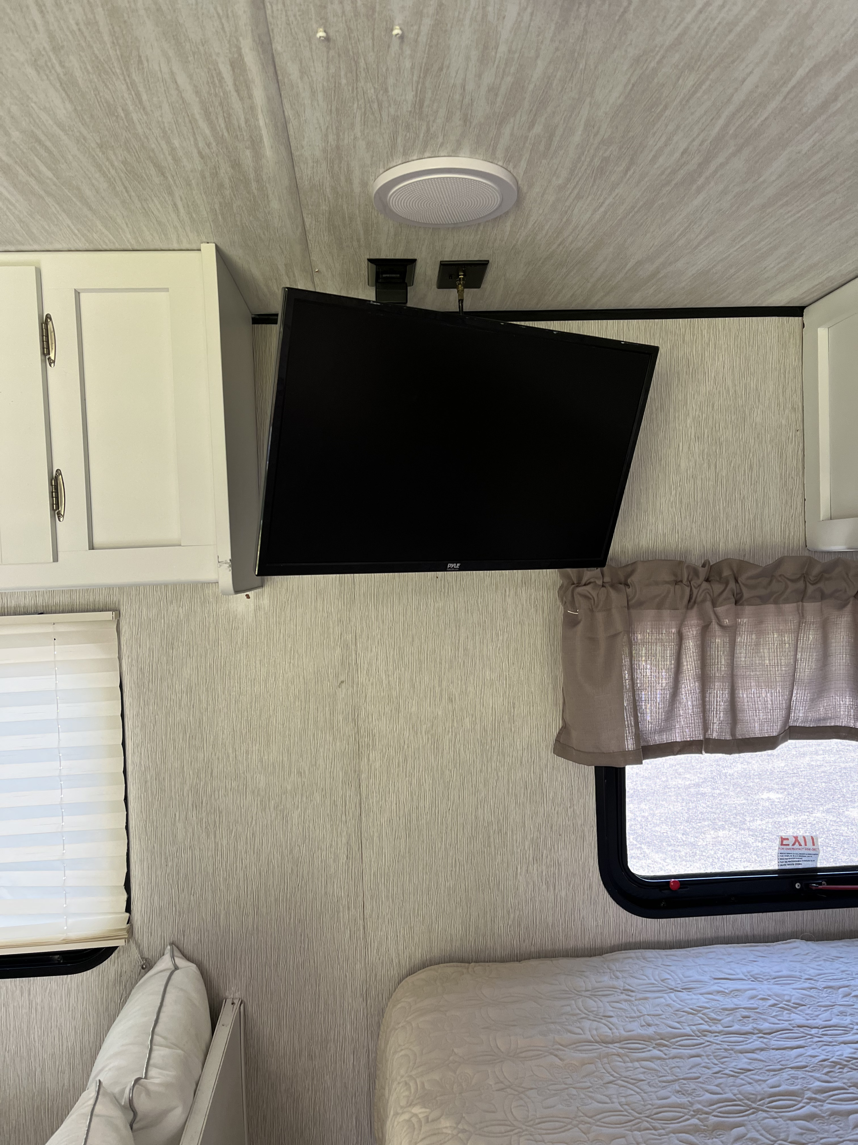 RV rental bedroom: wall-mounted TV, white cabinets, window, and bed in a compact, textured space.. Heartland RVs Pioneer 2019