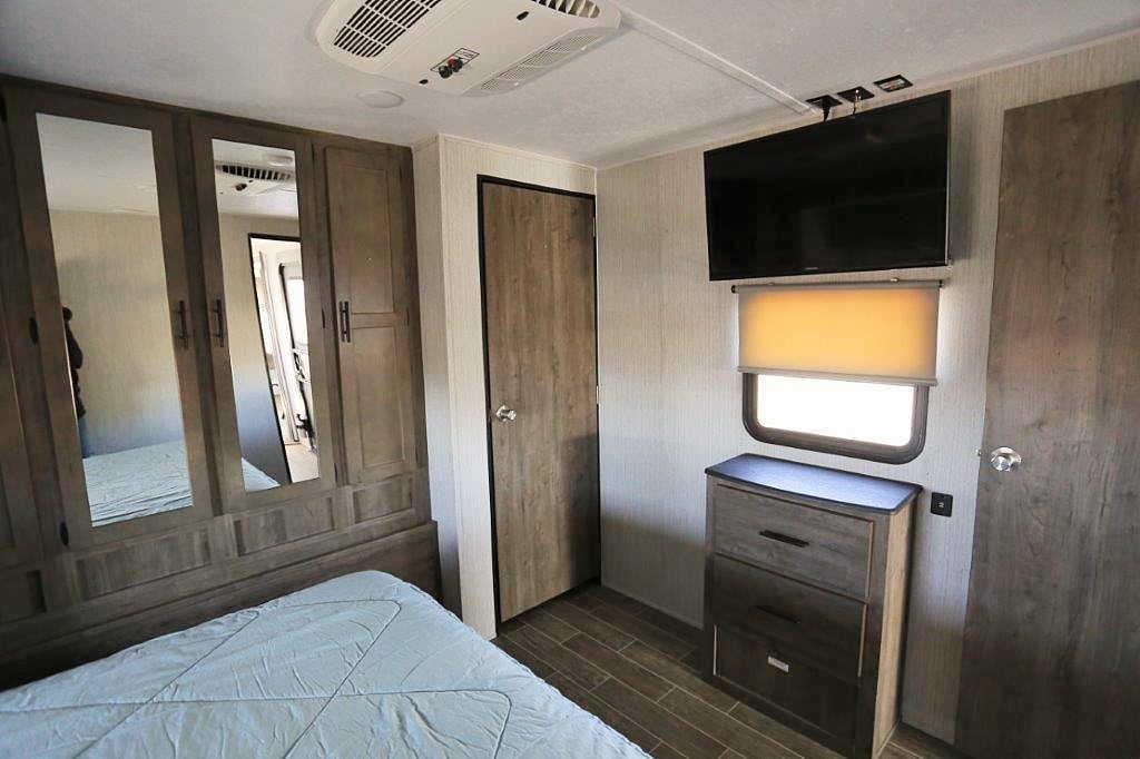 RV rental bedroom interior featuring a comfortable bed, mirrored wardrobe, TV, dresser, and a private door.. Palomino Puma 31-RLQS 2021