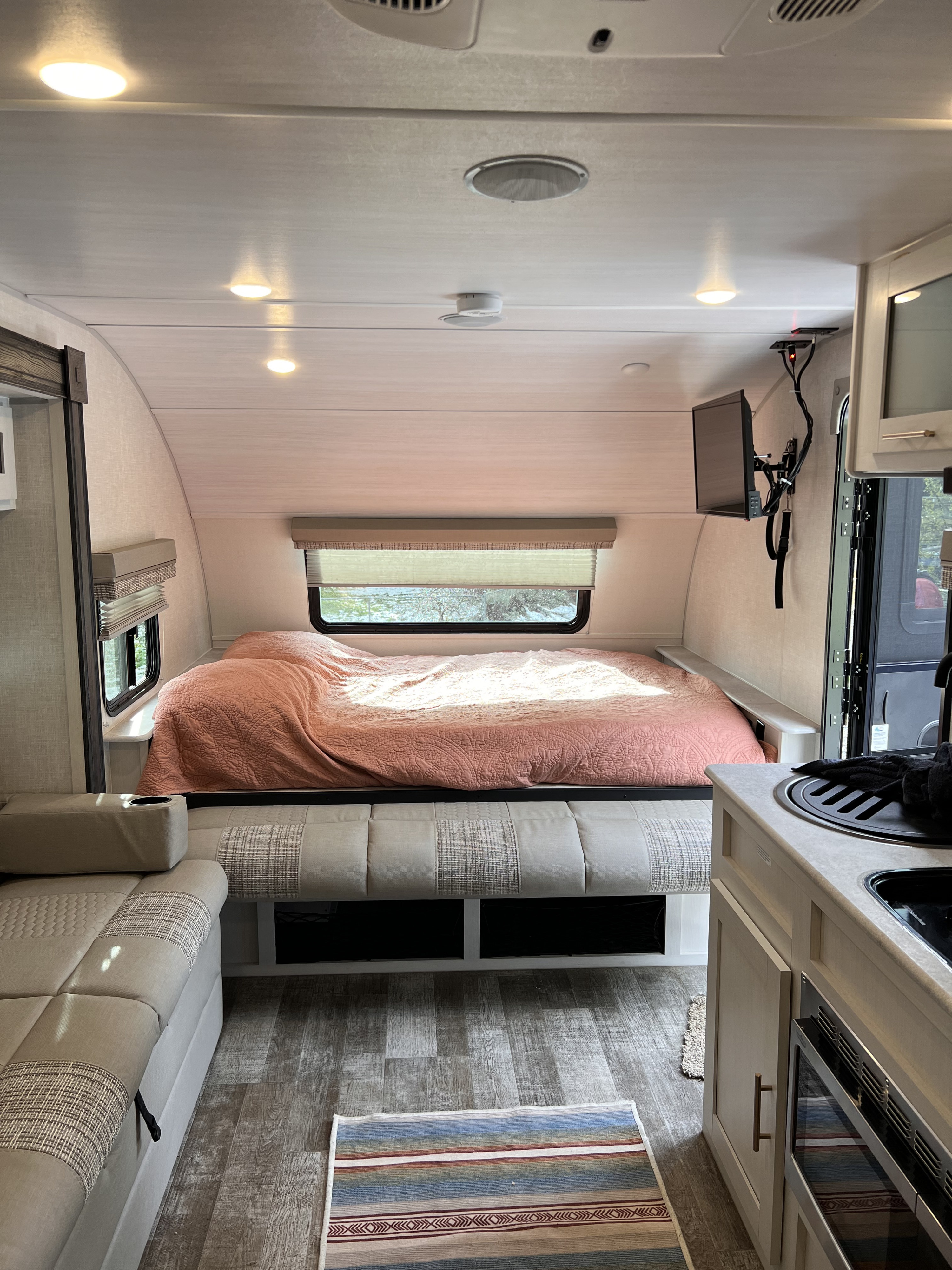 Cozy RV rental interior: view of the bed with pink comforter, seating area, small kitchen, and mounted TV.. R-Pod Hood River Edition 2021