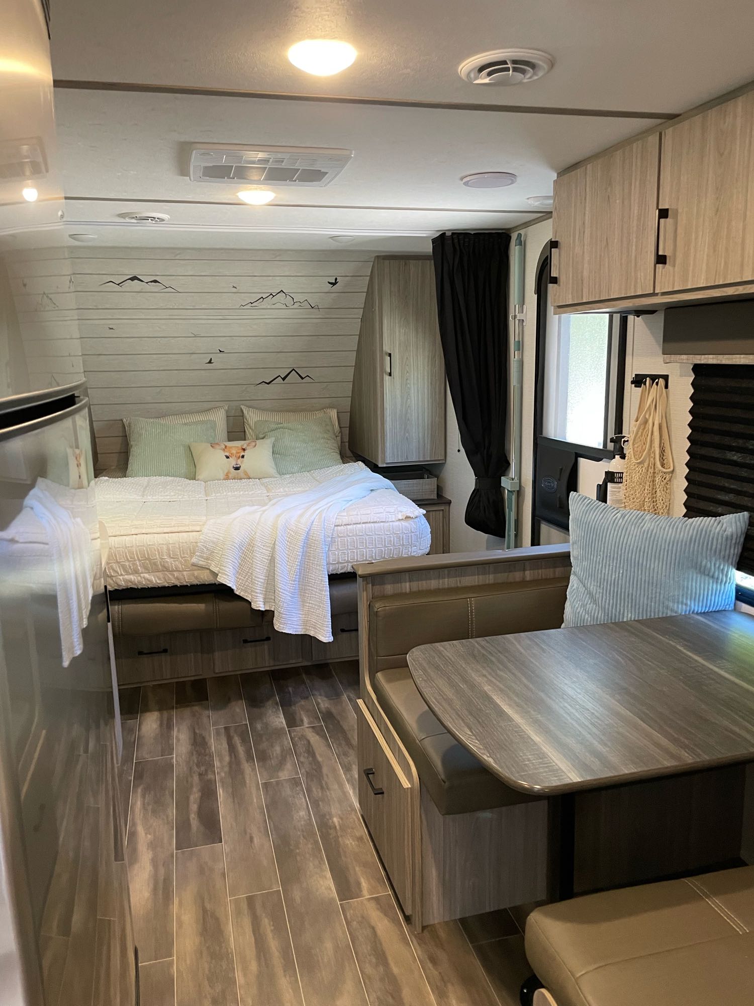 Bright RV rental living space featuring a comfy bed with decorative wall accents, a dining table, and wood-look floors.. Keystone RV Passport SL 2021