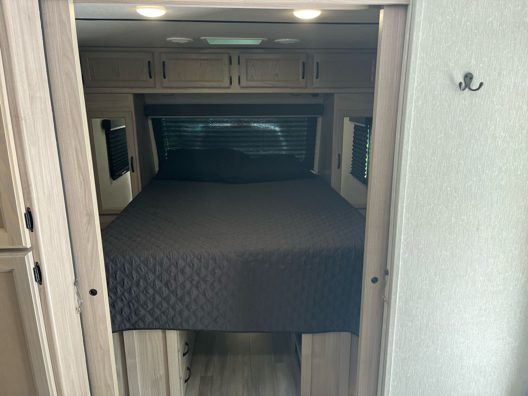 An RV rental bedroom interior, featuring a dark grey bed, overhead cabinets, mirrored side closets, and window blinds.. Coachmen 2549 BHX 2021