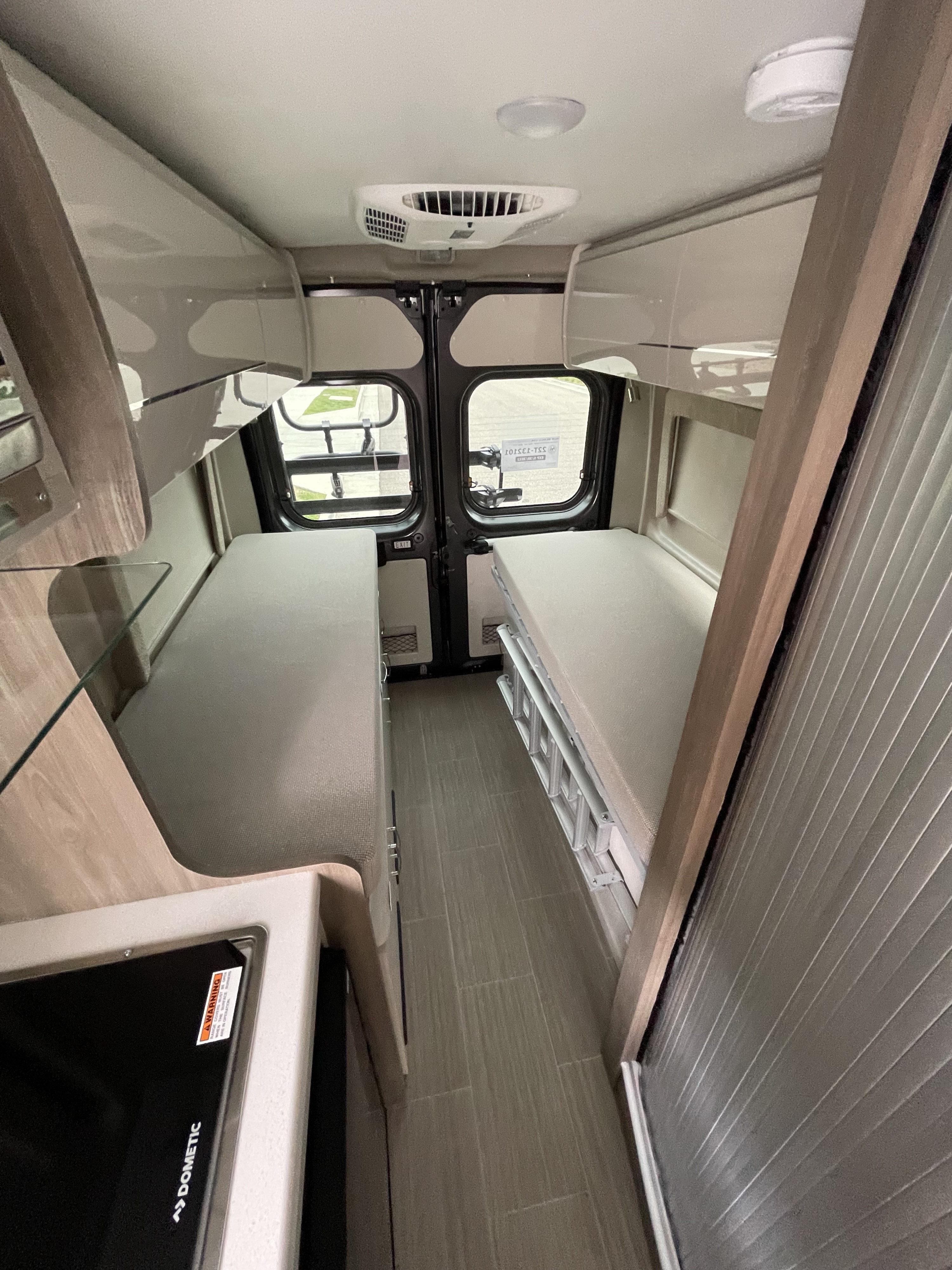 Cozy RV rental interior with twin beds, a compact kitchen, and overhead storage, ideal for road trips.. Thor Tellaro 2022