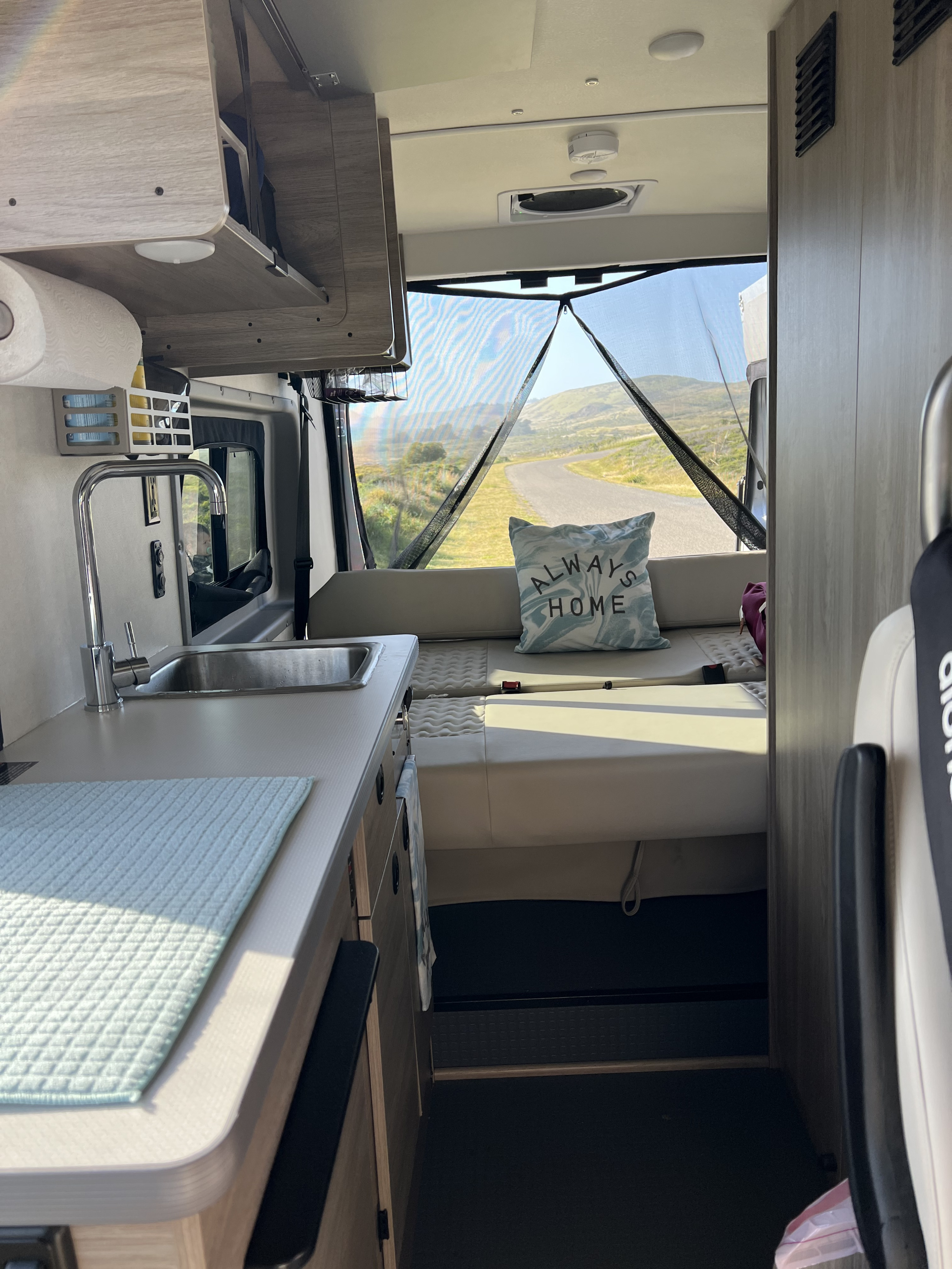Cozy rv rental interior featuring a practical kitchenette, comfy seating, and a mesh-screened rear door opening to a scenic road.. Winnebago Solis BUT59P 2024