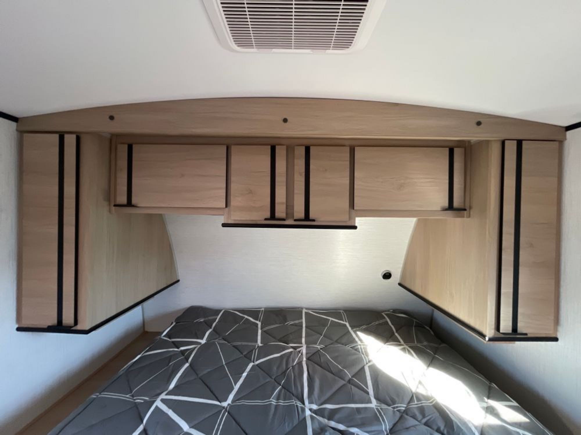 RV rental interior: Comfortable bedroom with light wood overhead cabinets and ceiling AC.. Cruiser Radiance 28QD 2022
