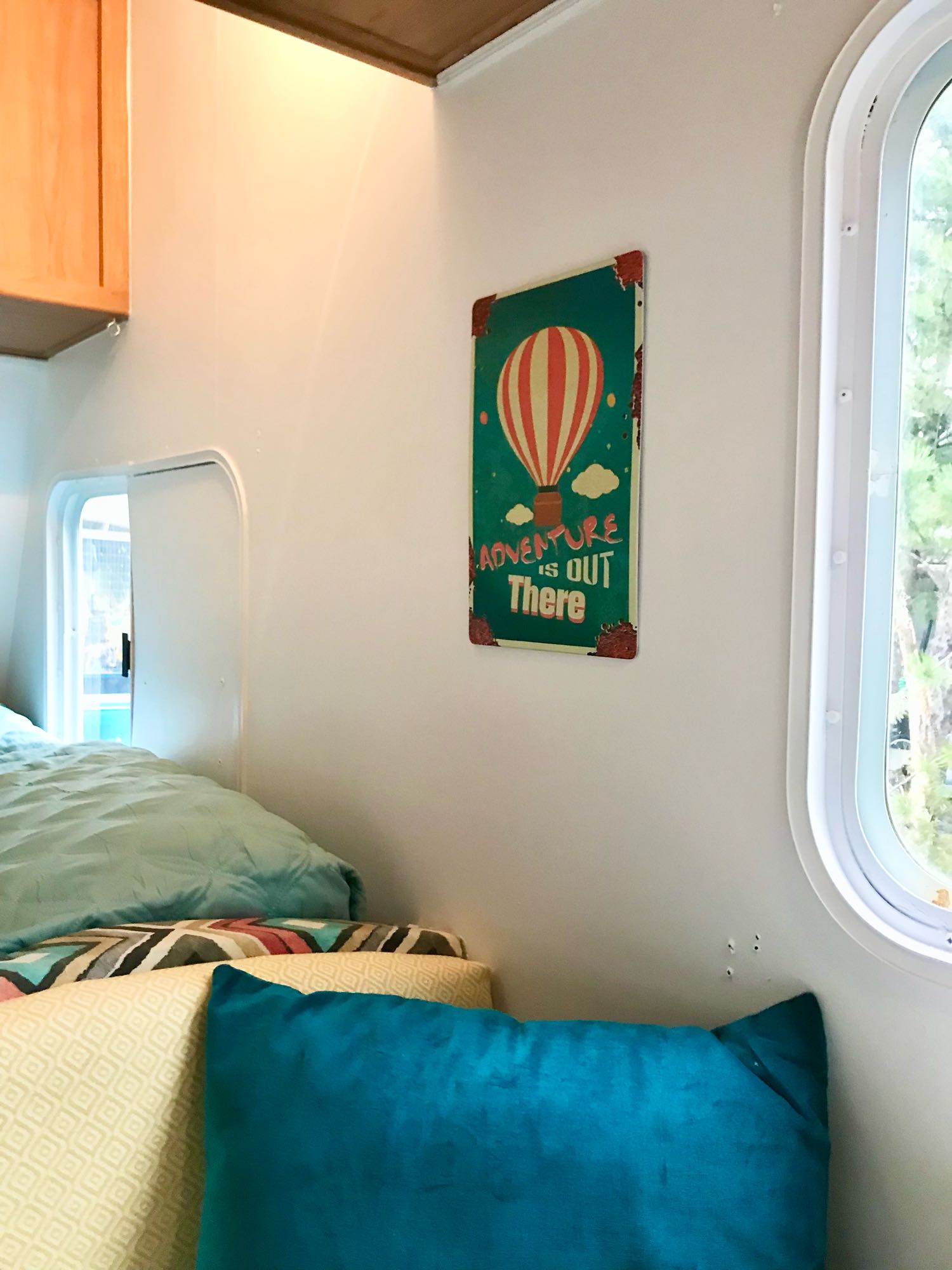 Cozy RV rental interior with a bright blue pillow, soft bed, window view, and an "Adventure is out There" sign.. Forest River Surveyor 2009