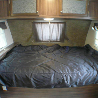 Spacious RV rental bedroom: dark comforter on a large bed, overhead wood cabinets. Perfect for your travel comfort.. Coachmen nano 2017