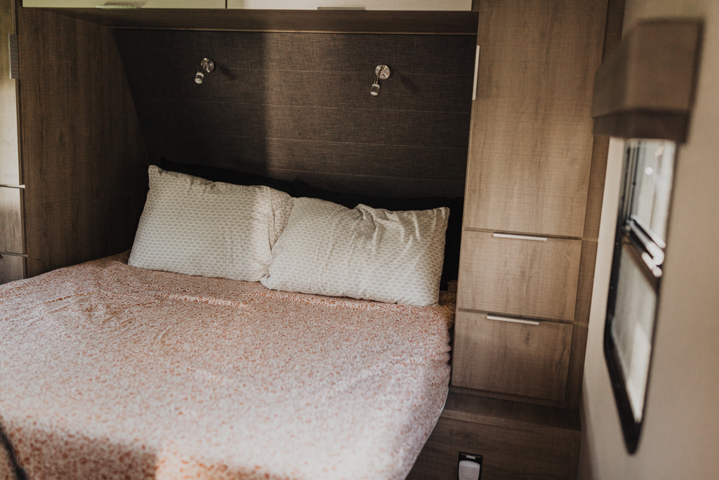 Comfortable RV rental bedroom: bed with patterned duvet, pillows, headboard lights, and wood storage cabinets.. Grand Design Imagine 2020