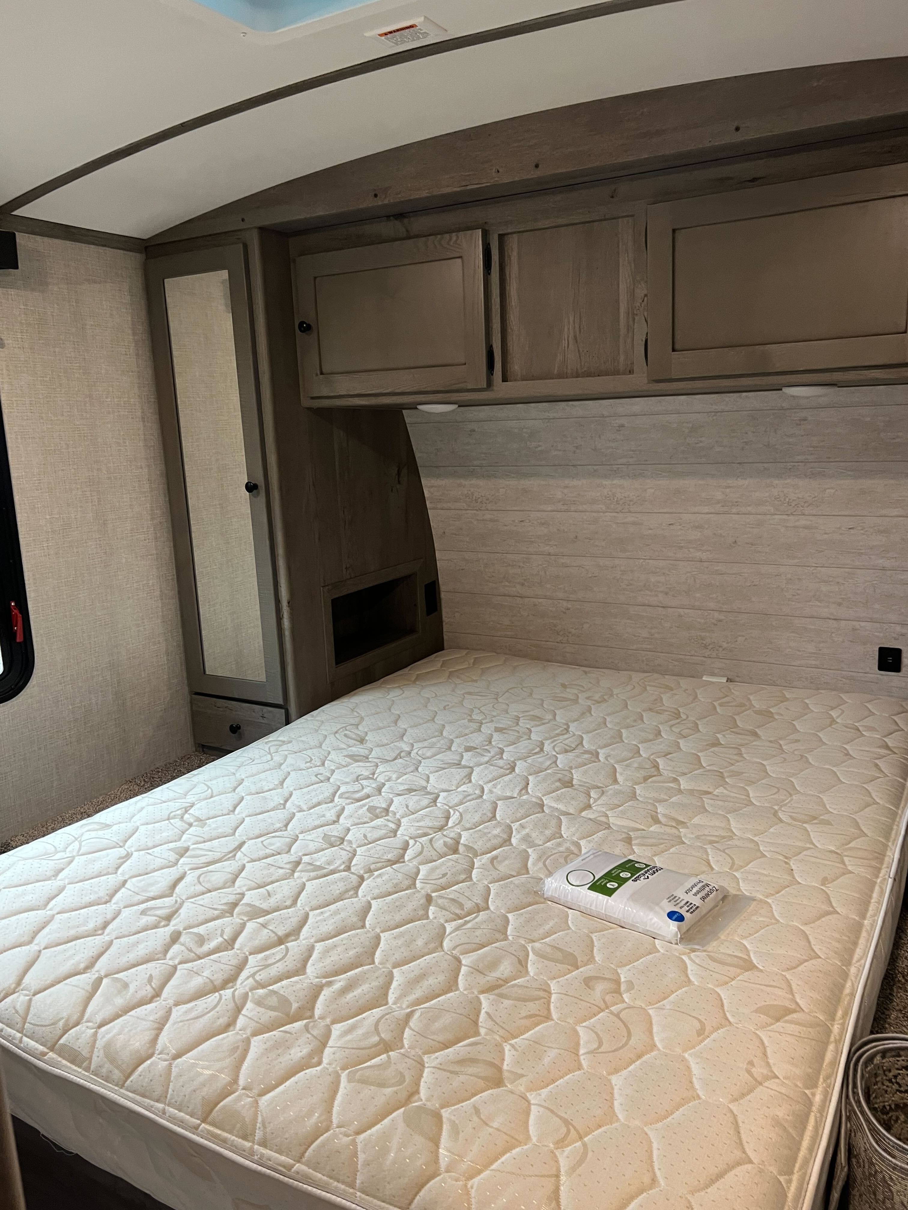 Experience comfort in this RV rental bedroom. It features a new mattress with protector, overhead cabinets, and a mirrored wardrobe.. Keystone Outback 2020