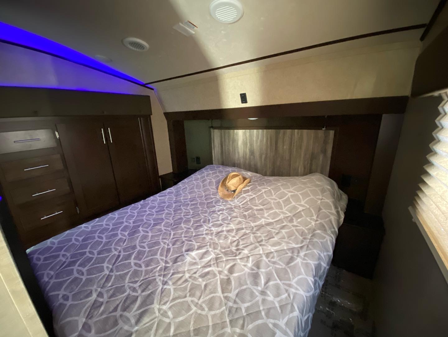 This RV rental bedroom features a queen-sized bed with patterned bedding, built-in dark wood cabinetry, and blue accent lighting.. Forest River Cherokee Arctic Wolf 2018