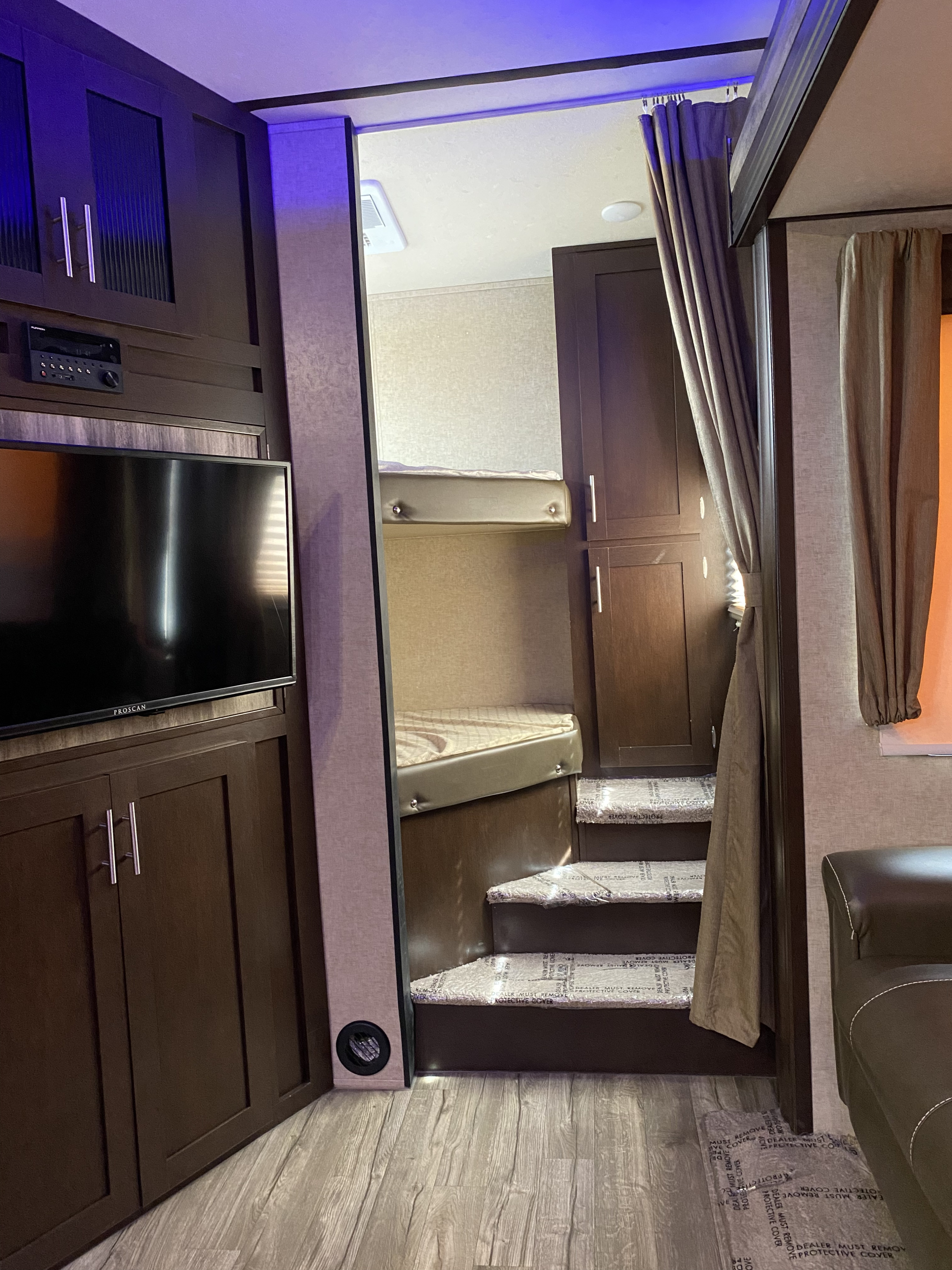 Inside this RV rental: Dark wood cabinetry, a TV, and steps with protective covers leading to bunk beds under blue accent lighting.. Forest River Cherokee Arctic Wolf 2018