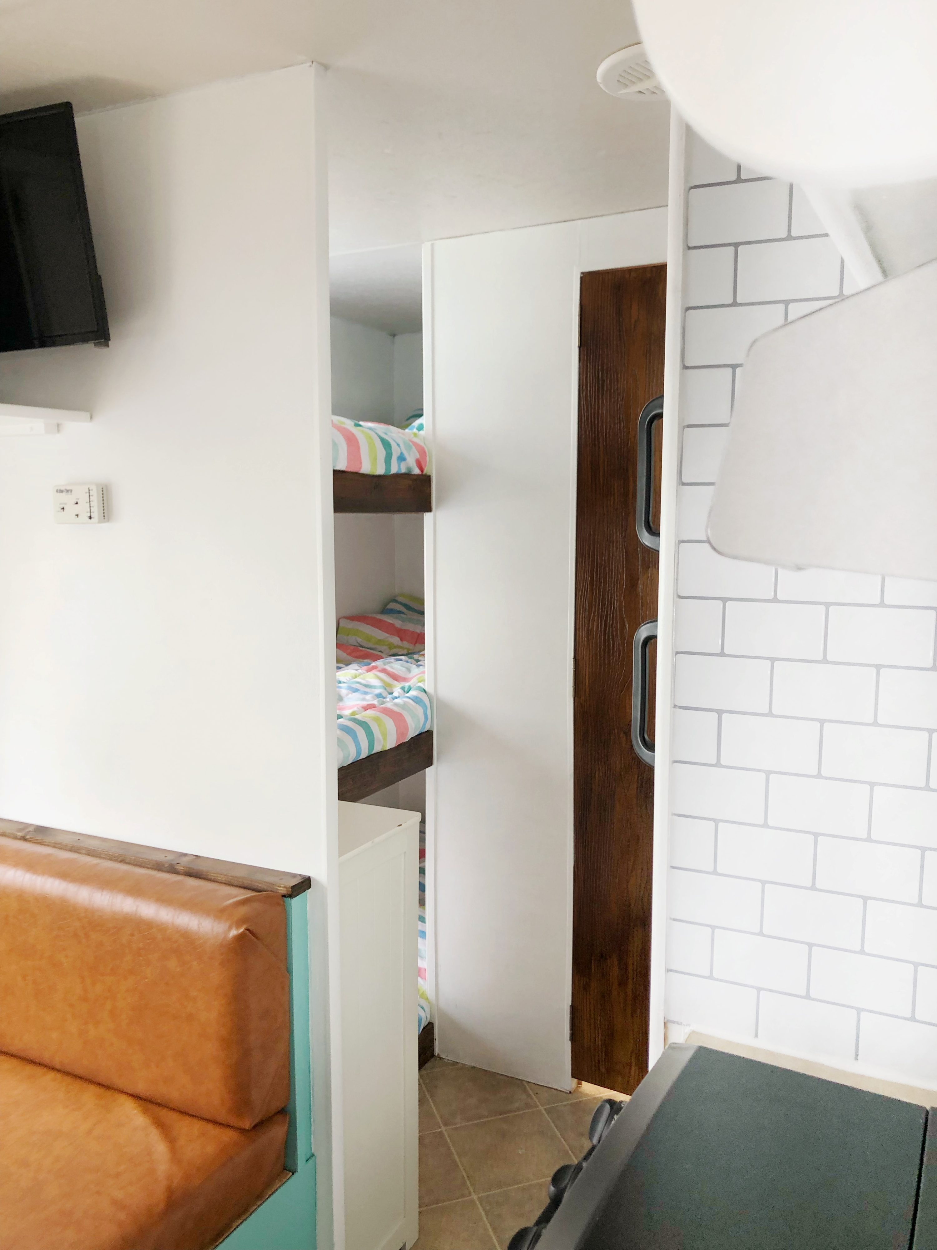 Modern RV rental interior: view of bunk beds with striped bedding, a cozy dining booth, and white brick accents.. Layton Layton Trailer 2006