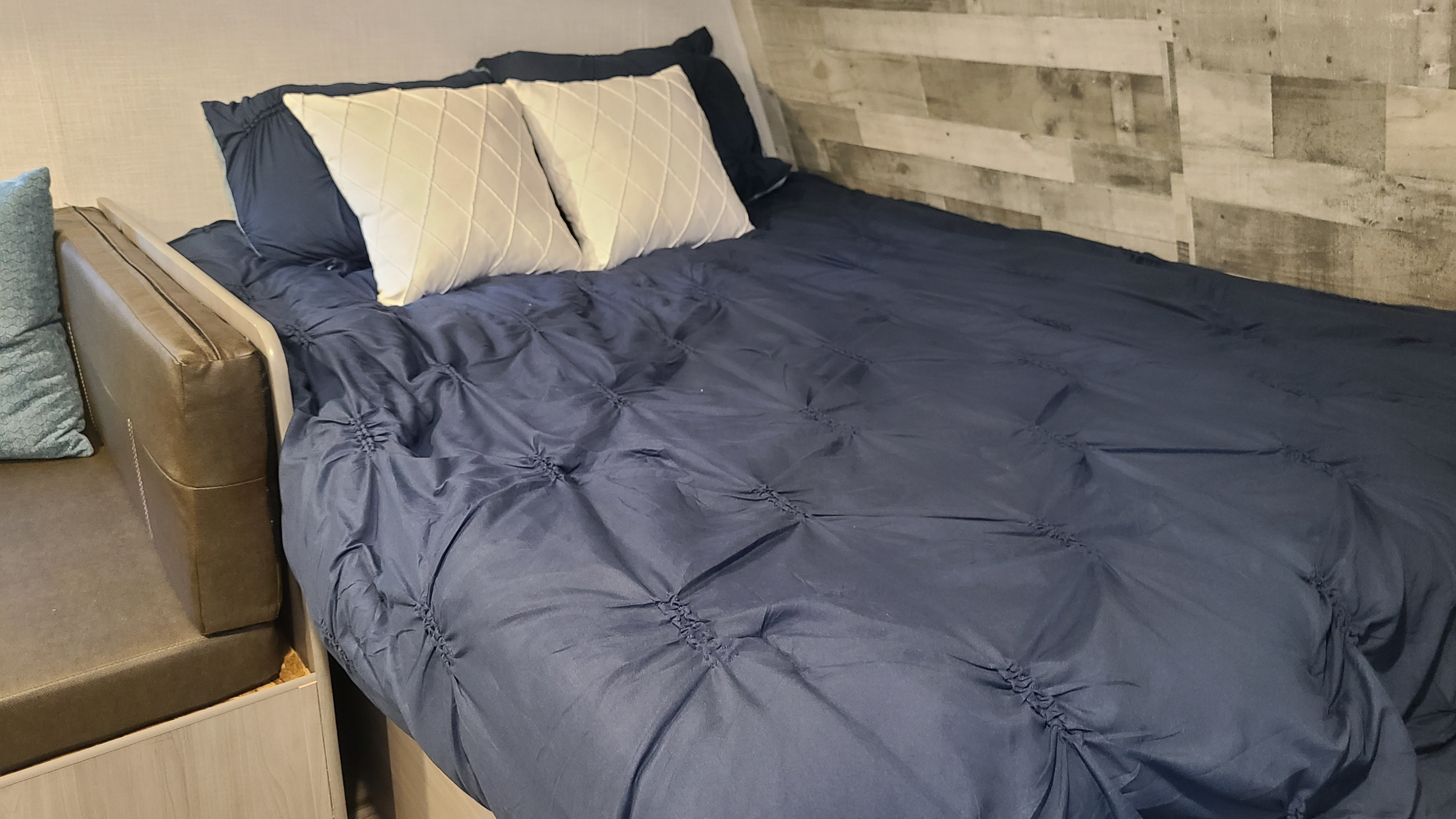 Inside an RV rental: a neatly made bed with blue comforter, white pillows, and wood accent wall. Comfortable travel accommodation.. Dutchman Coleman Lantern LT 17B 2022