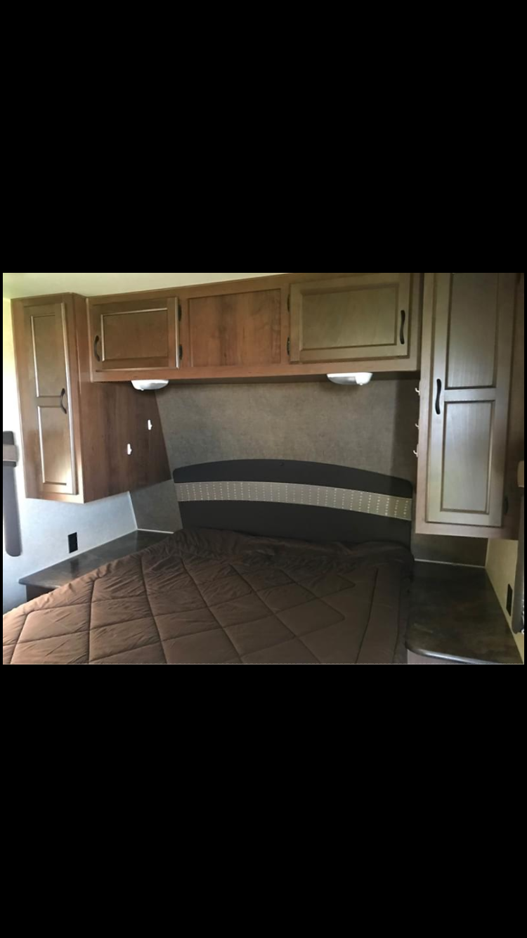 Cozy and compact RV rental bedroom featuring a brown bed, patterned headboard, and wood overhead cabinets.. Jayco Coyote 2014