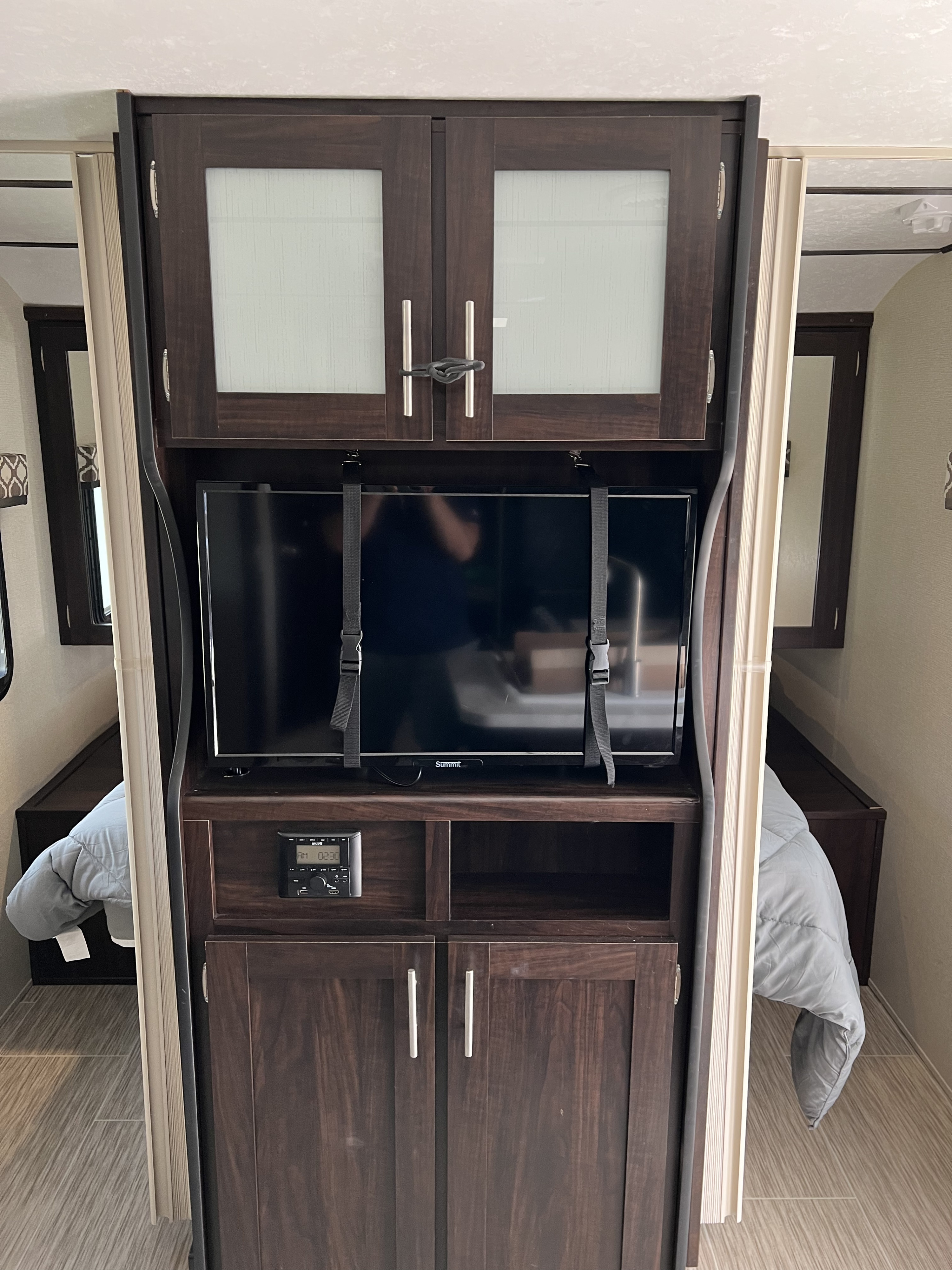 View of an RV rental's entertainment unit, showcasing a TV secured with straps, cabinets, and compact sleeping areas.. Forest River Tracer Breeze 2018