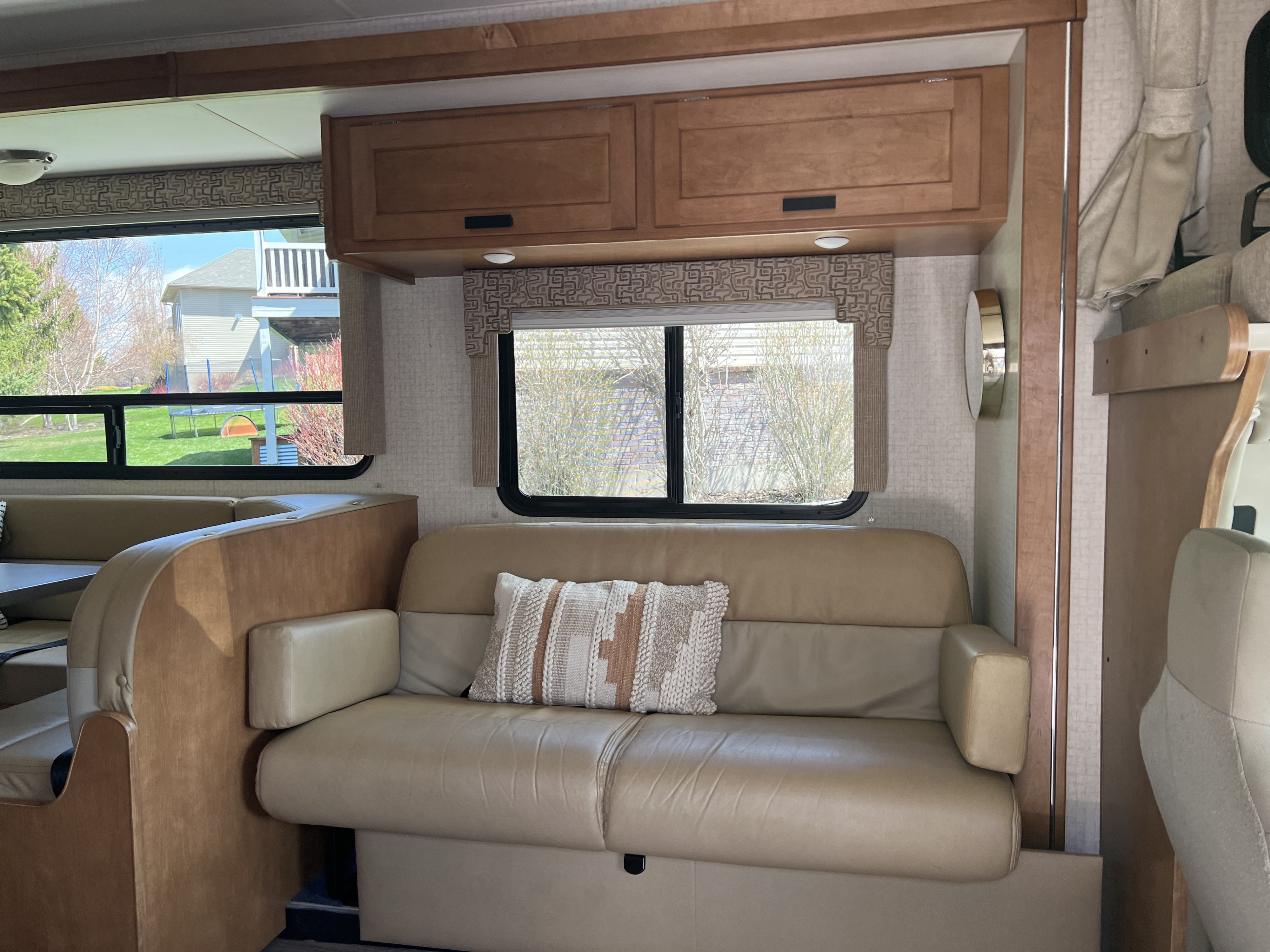 Cozy RV rental living space with a tan sofa, wood cabinets, and large windows showing a backyard.. Winnebago Minnie Winnie 2017