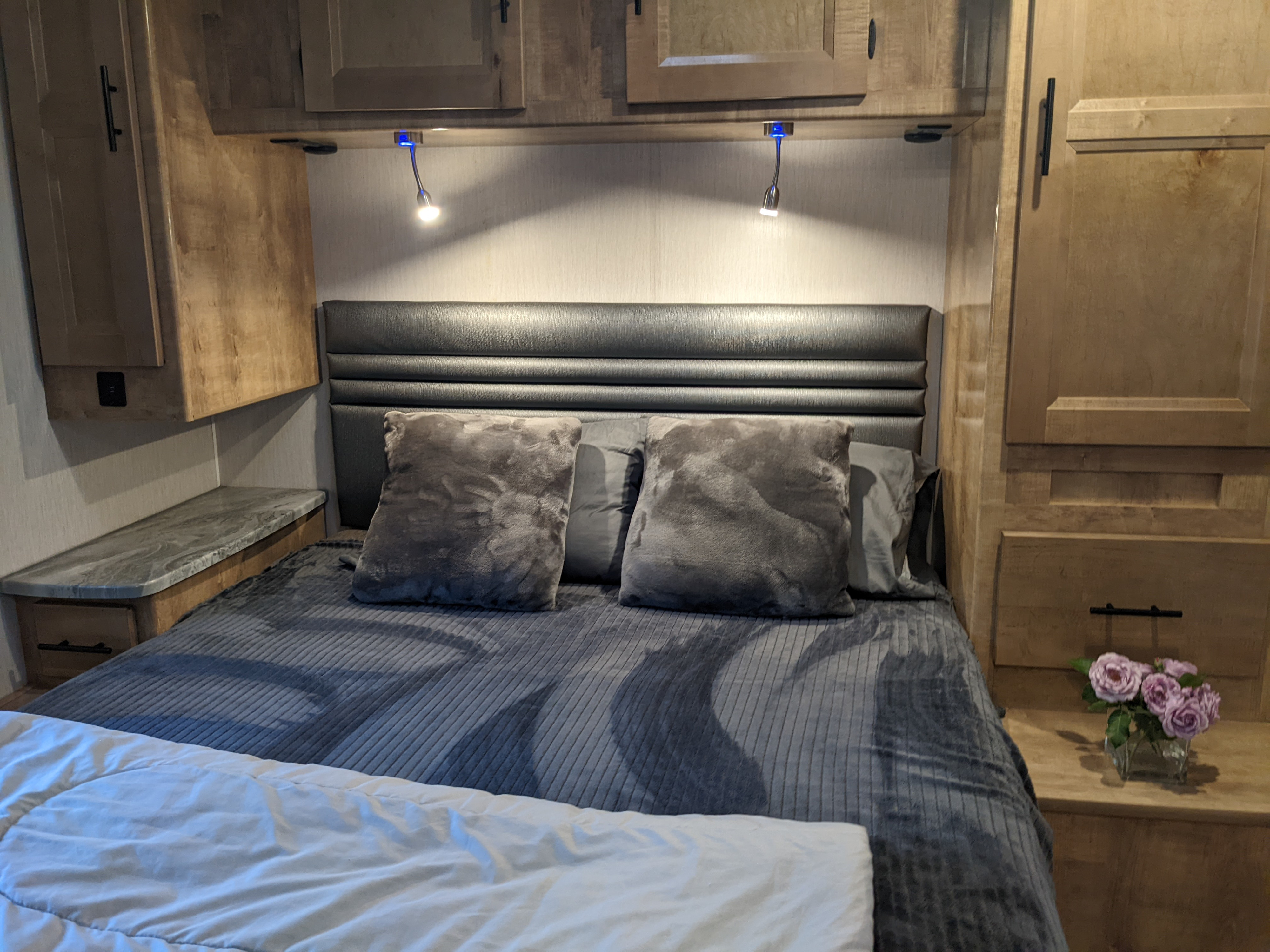 Cozy RV rental bedroom with a comfortable bed, integrated storage, reading lights, and a small nightstand for convenience.. Coachmen Leprechaun 2021