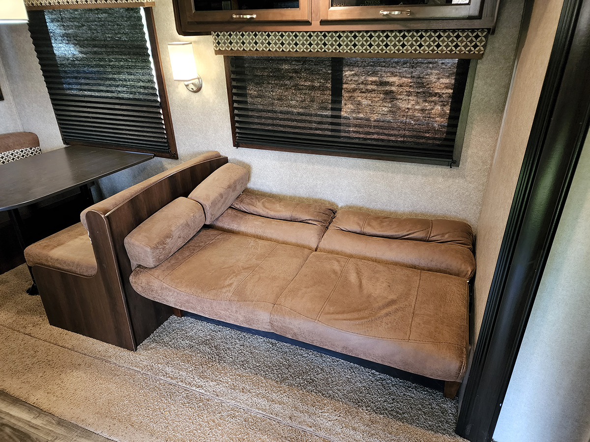 Compact RV rental living space: Brown sofa bed extended for sleeping, with a nearby dining booth table.. Jayco Jay Flight SLX Rocky Mountain Edition 2018