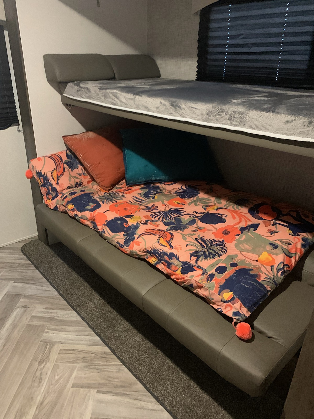 RV rental offers bunk beds: a grey top bunk & a lower sofa-sleeper with colorful floral bedding & pillows.. Forest River EVO 3250 2021