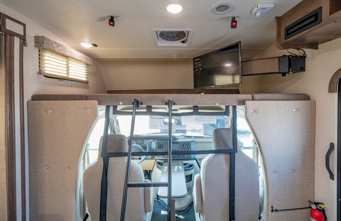 RV rental interior features: over-cab bunk bed with ladder, front cockpit area with swivel seats, and TV.. Coachmen Freelander 28BH 2018