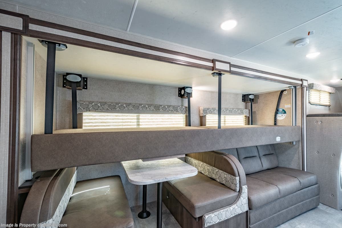 RV rental interior: comfortable layout with an upper bunk bed, dinette with table, and sofa seating. Seatbelts visible.. Coachmen Freelander 28BH 2018