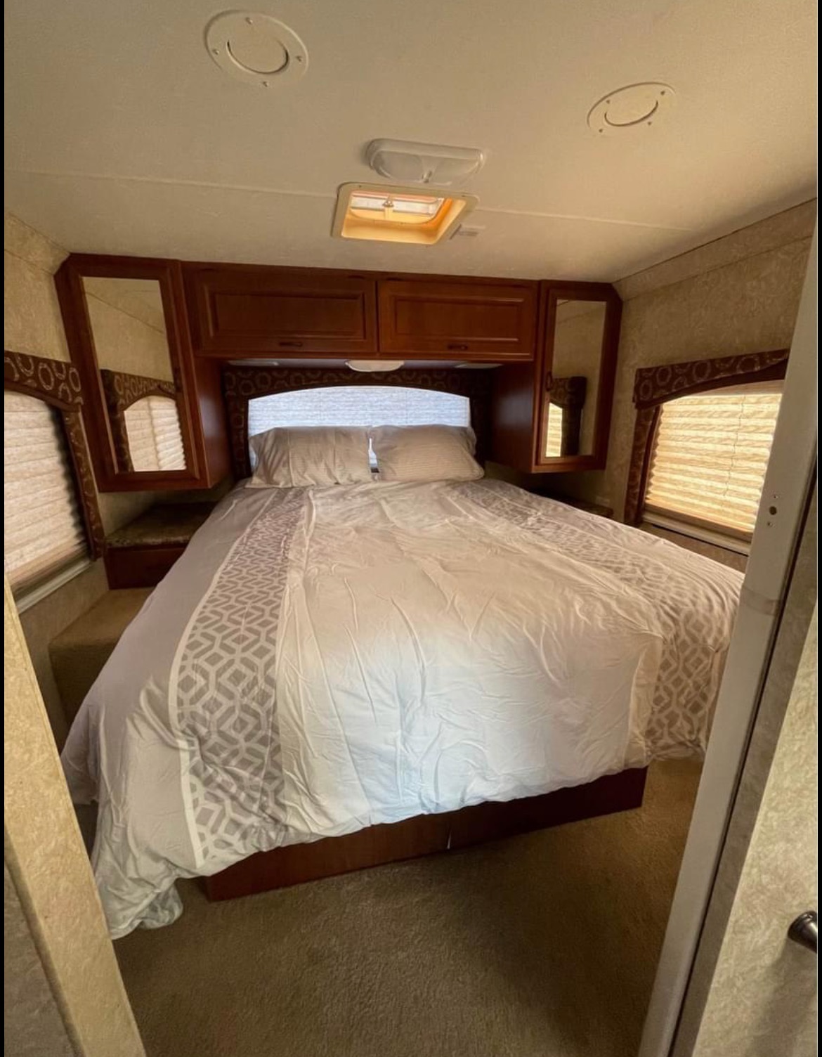 Spacious RV rental bedroom with a comfortable bed, overhead cabinets, and windows with blinds. Ready for your adventure.. Four Winds Hurricane 2011