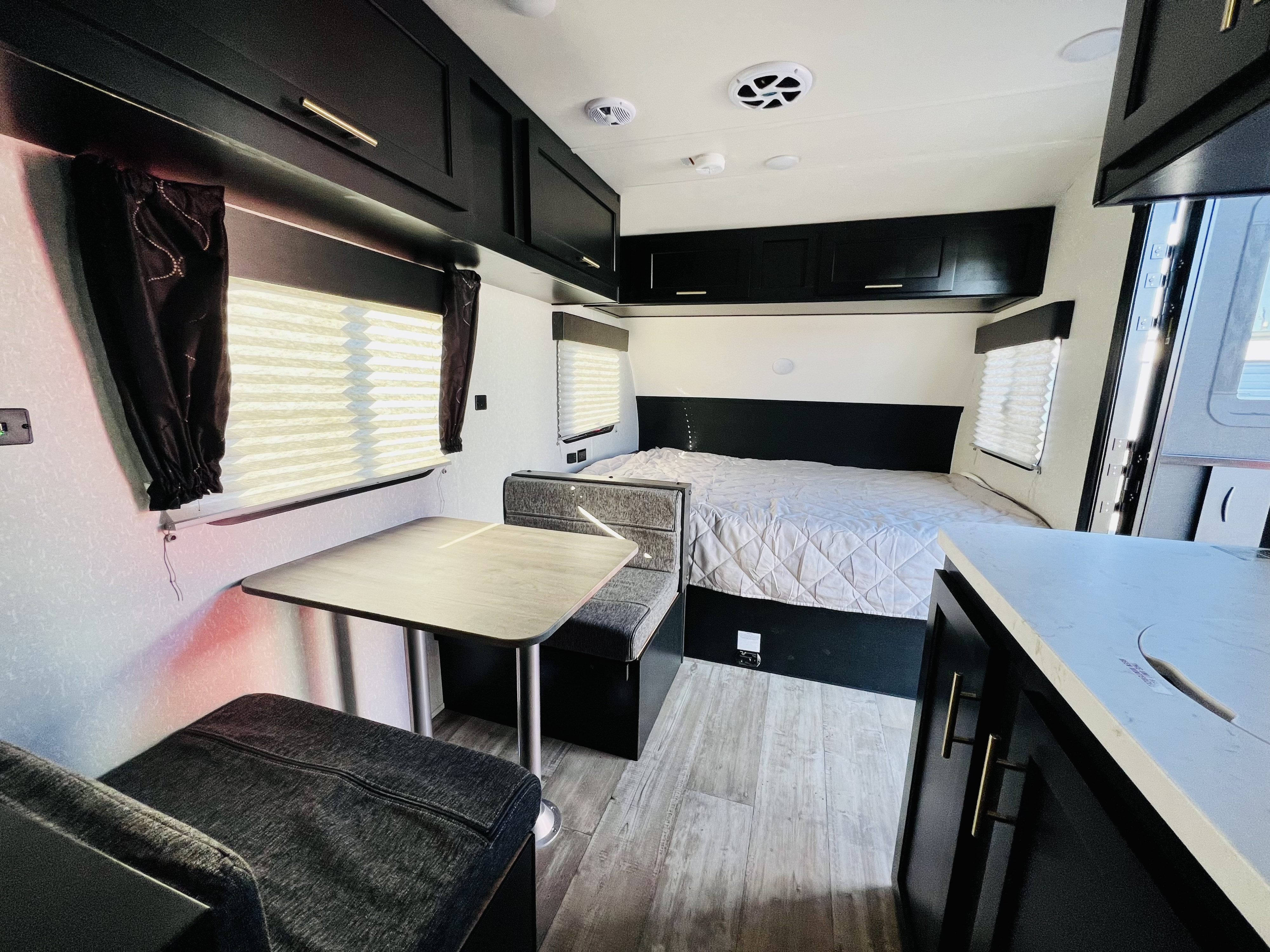 Rv rental interior with a bed, dinette, black overhead cabinets with gold pulls, and light wood-patterned flooring.. Forest River Cherokee Wolf Pup 2022