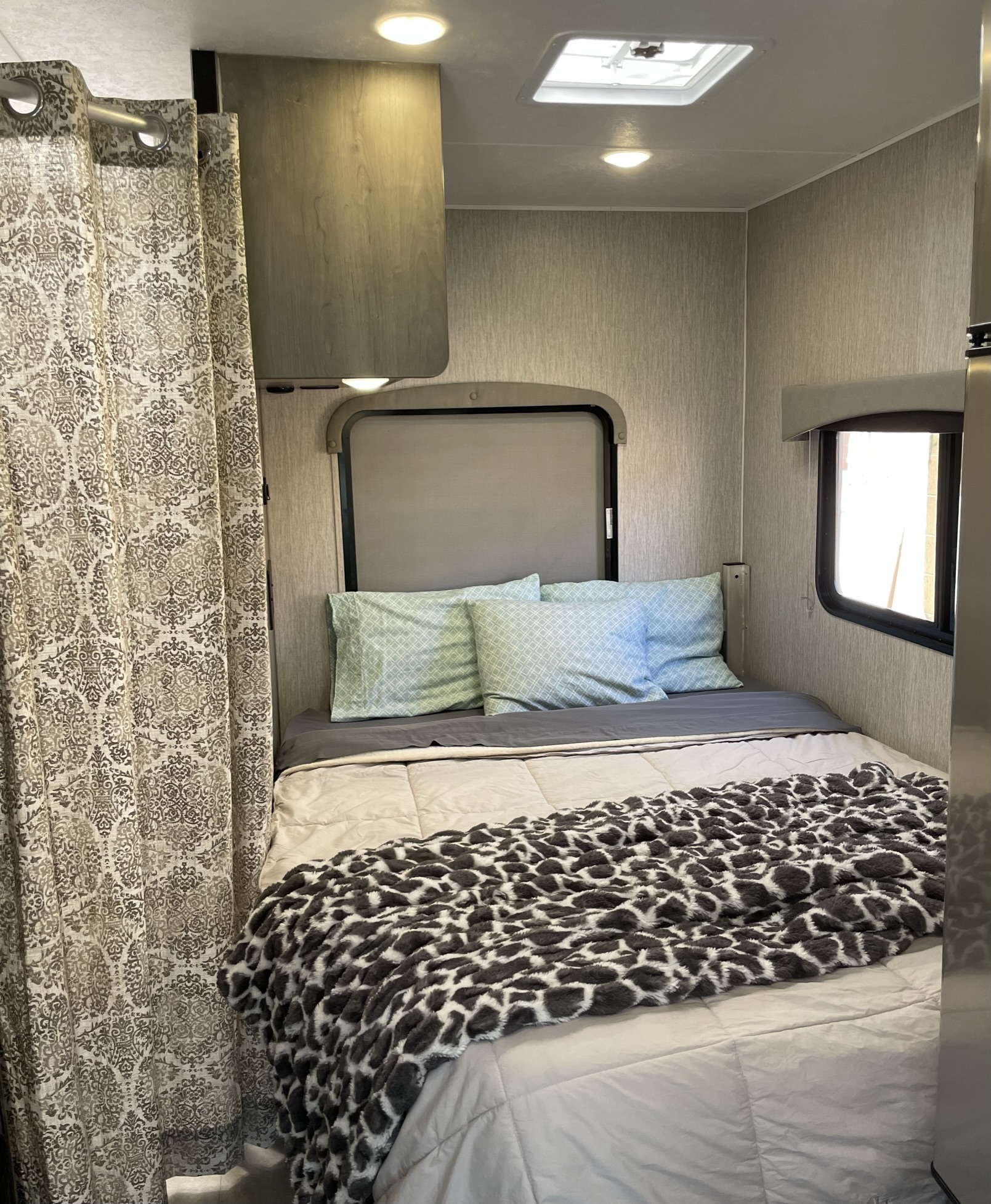 Cozy RV rental bedroom features a bed with patterned blanket, light blue pillows, privacy curtain, and overhead lights.. Coachmen Freelander 22QB 2022