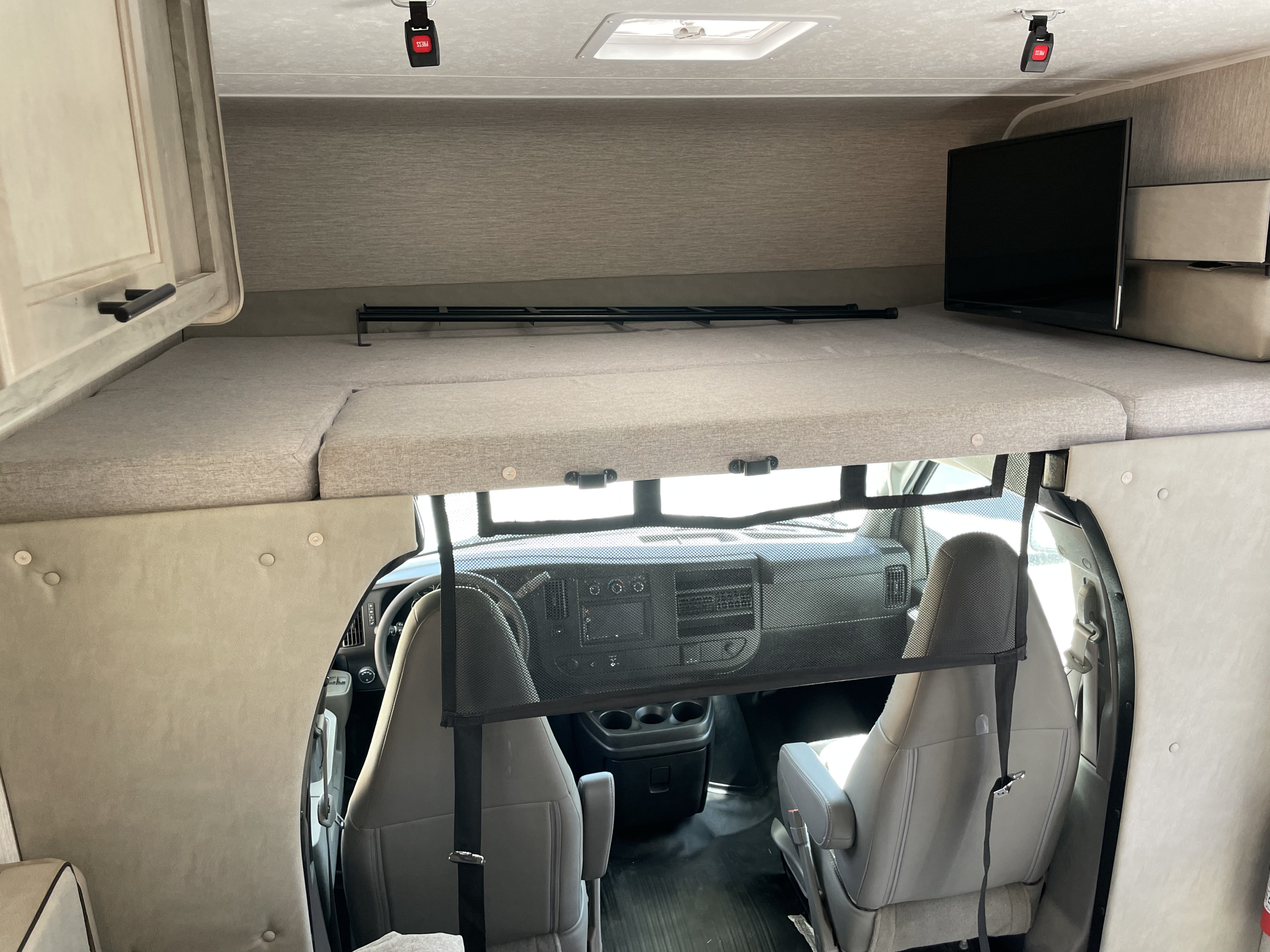 RV rental interior showing a cab-over bunk bed with TV, ladder, and safety netting above the vehicle's cockpit.. Coachmen Freelander 22QB 2022