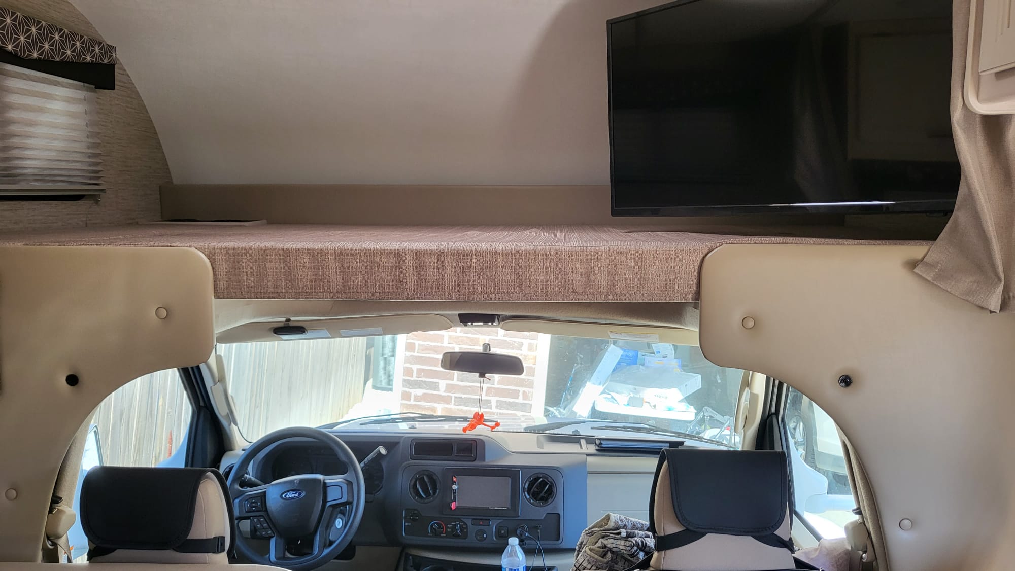 Inside an RV rental: view of the cab-over bunk, mounted TV, and driver's cockpit for your next motorhome adventure.. Ford Freedom Elite 2022