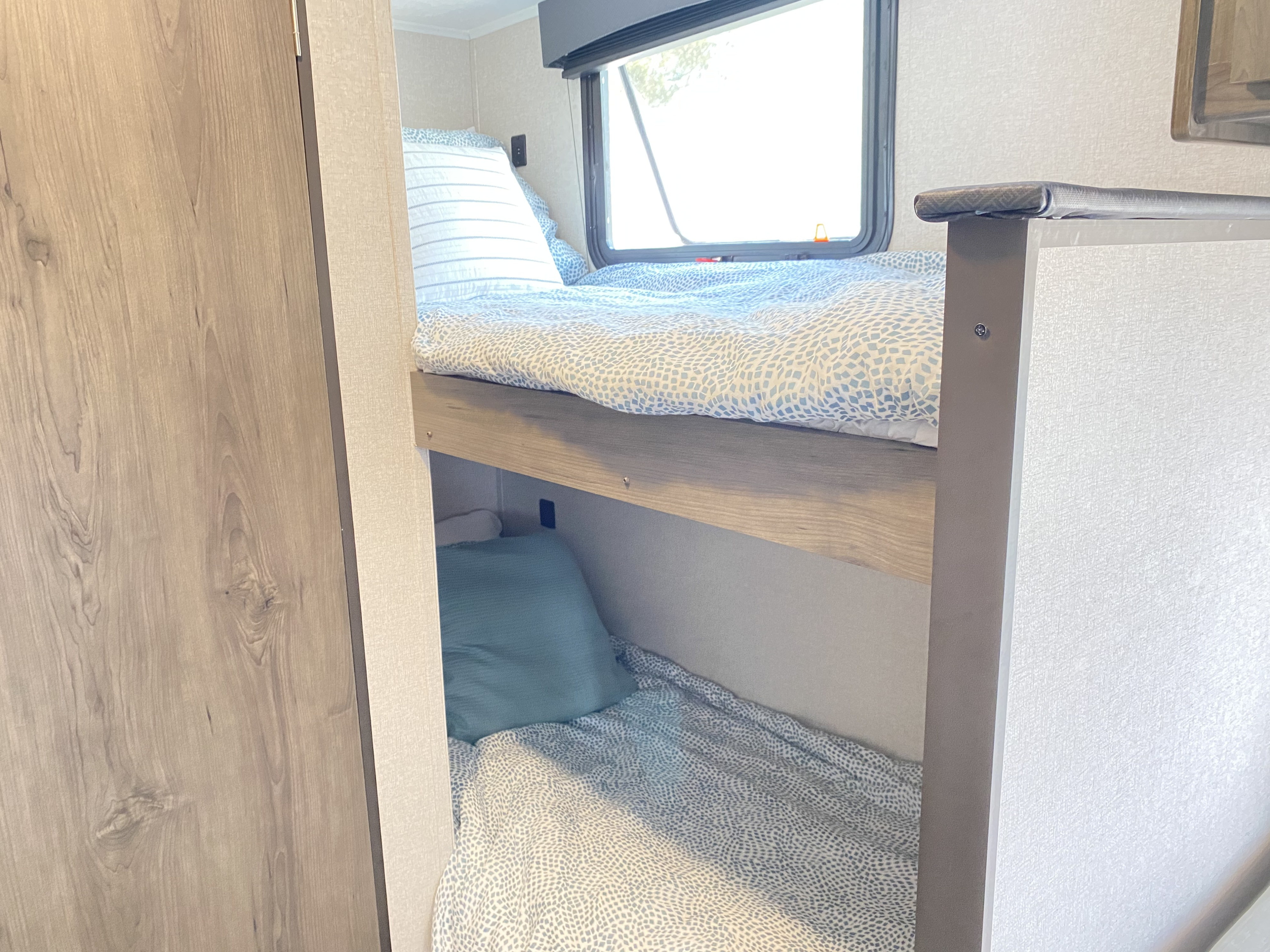Inside this **RV rental**, comfortable bunk beds with blue bedding and a window offer a cozy sleeping space.. Forest River Clipper Cadet 2021