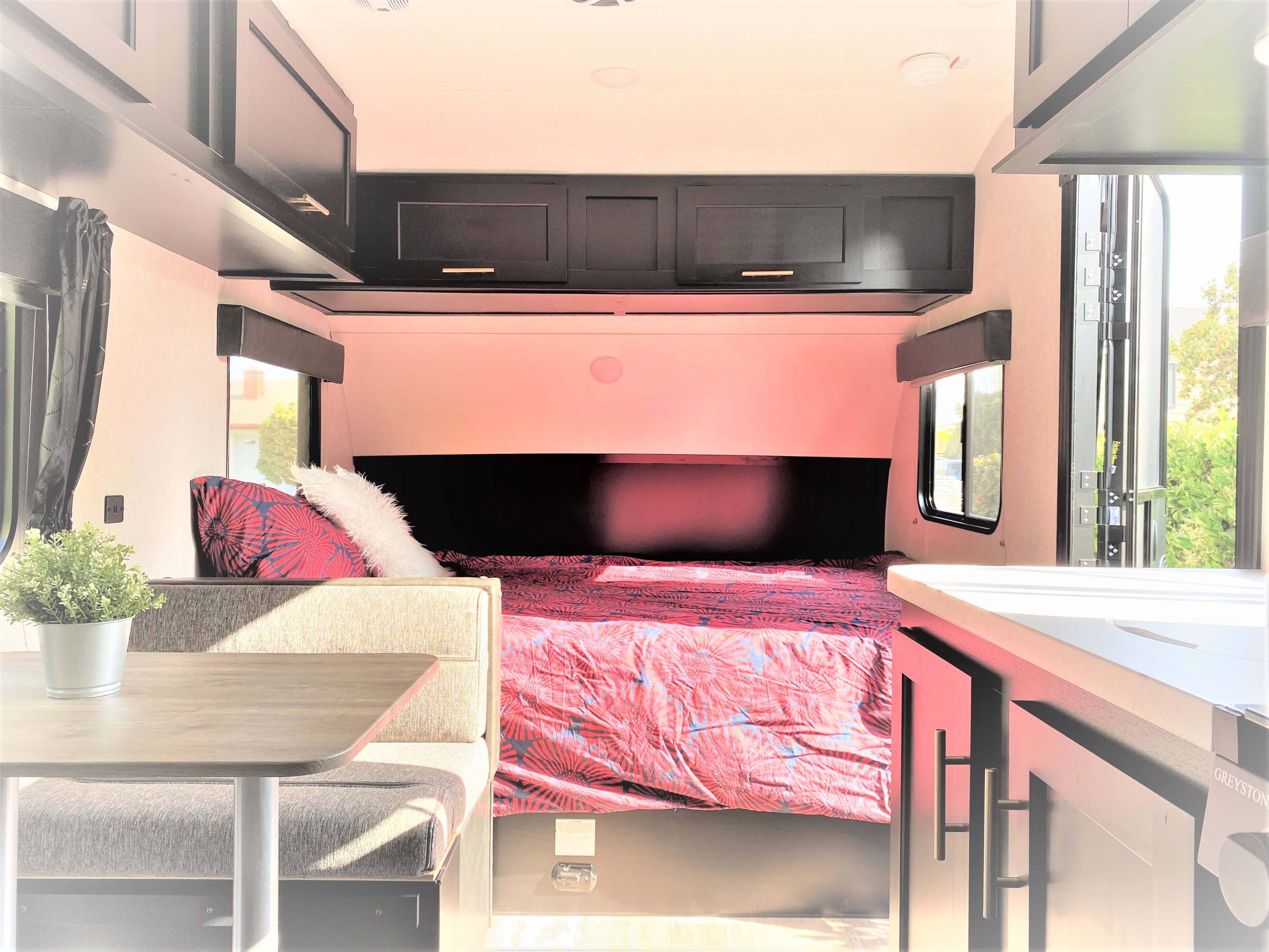 Bright rv rental interior with a bed, dining nook, and dark overhead cabinets, offering a functional living space.. Forest River Cherokee Wolf Pup 2021