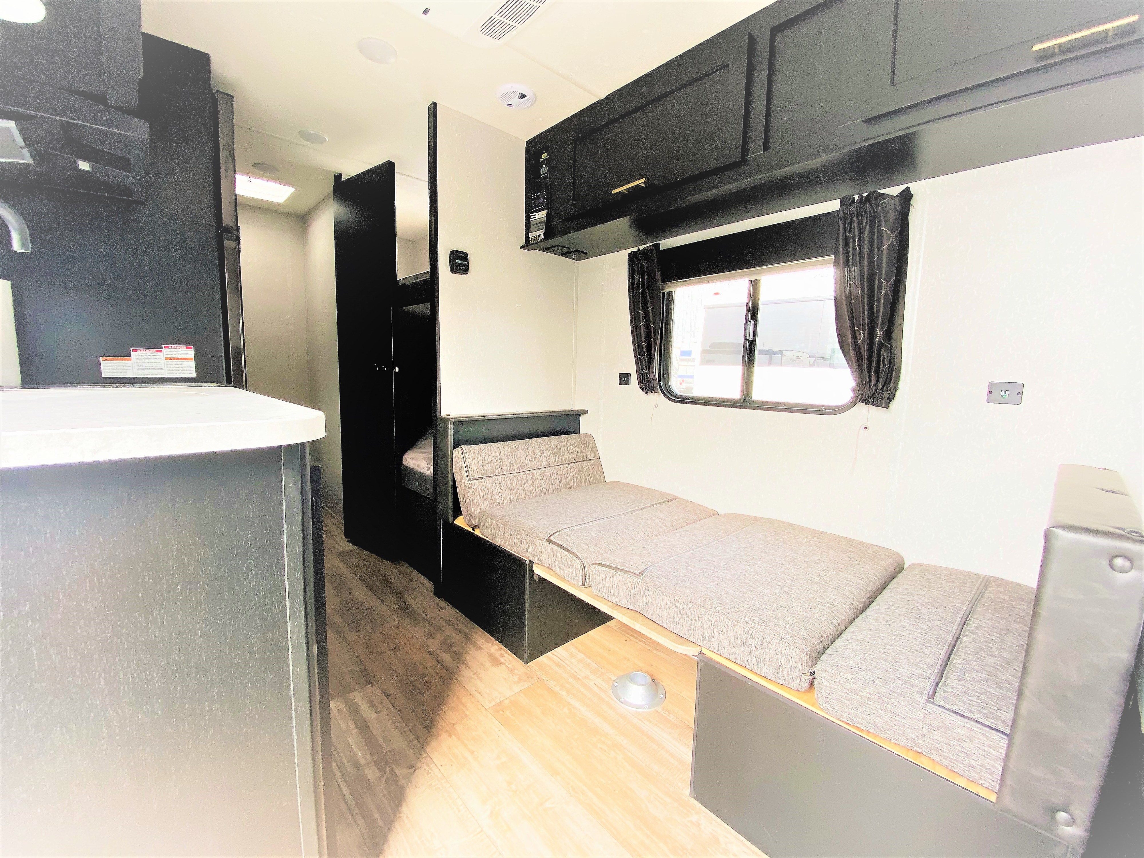 This rv rental interior features a convertible sofa bed, overhead cabinets, and bunk beds, offering a cozy and functional space.. Forest River Cherokee Wolf Pup 2022