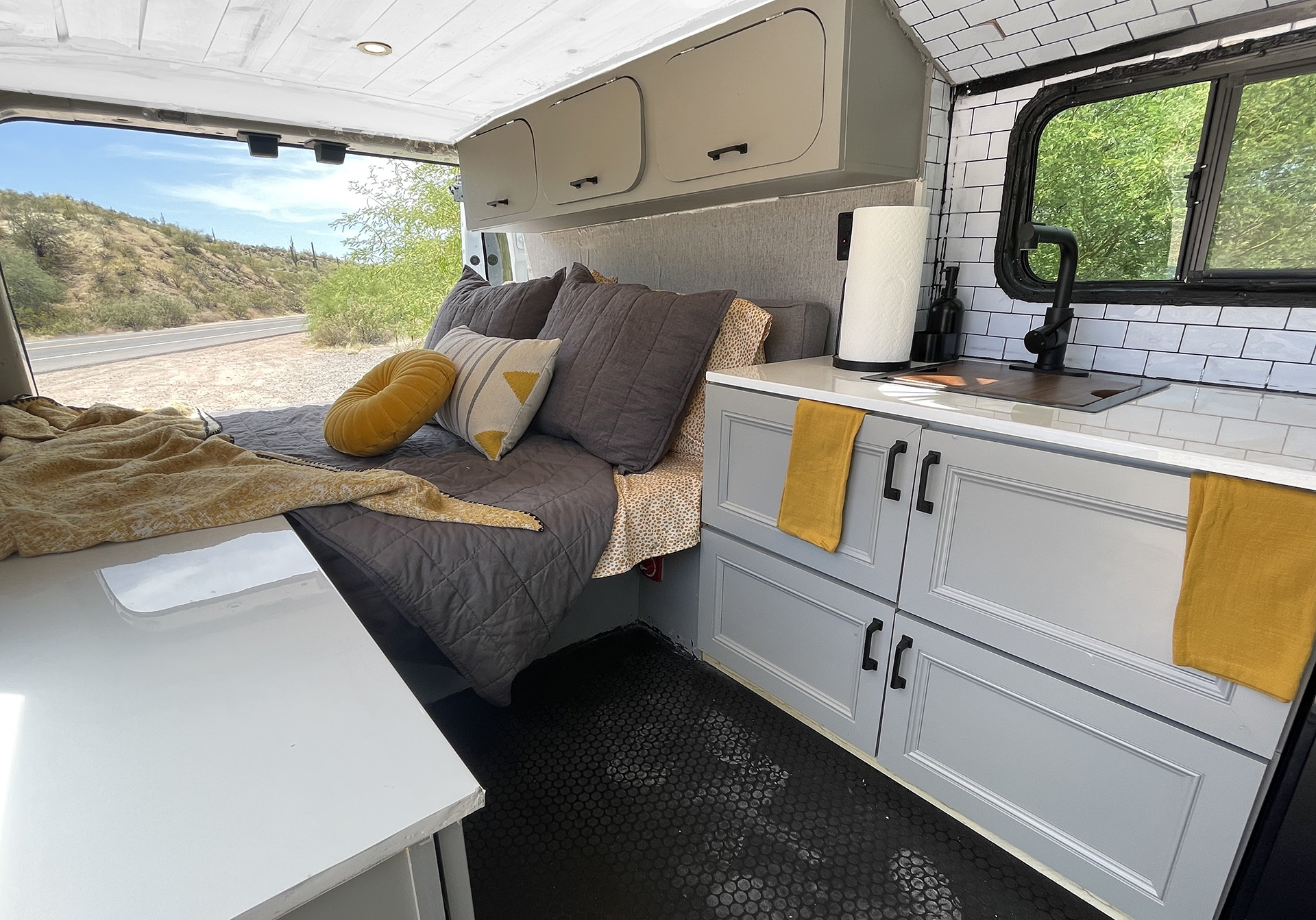 Modern rv rental interior with a cozy bed, fully equipped kitchenette, and desert views. Black hexagonal floor & stylish storage.. Ford Transit 2015