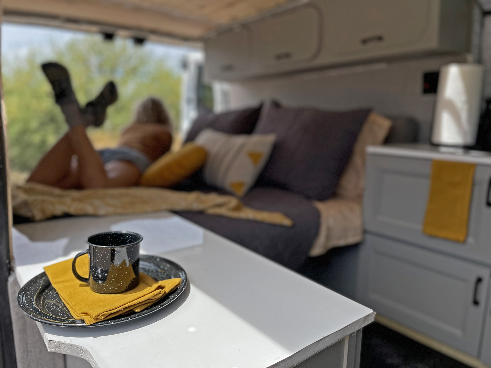 Relaxed rv rental interior with a speckled mug on a table. A person lies on the bed, legs up, enjoying the view.. Ford Transit 2015