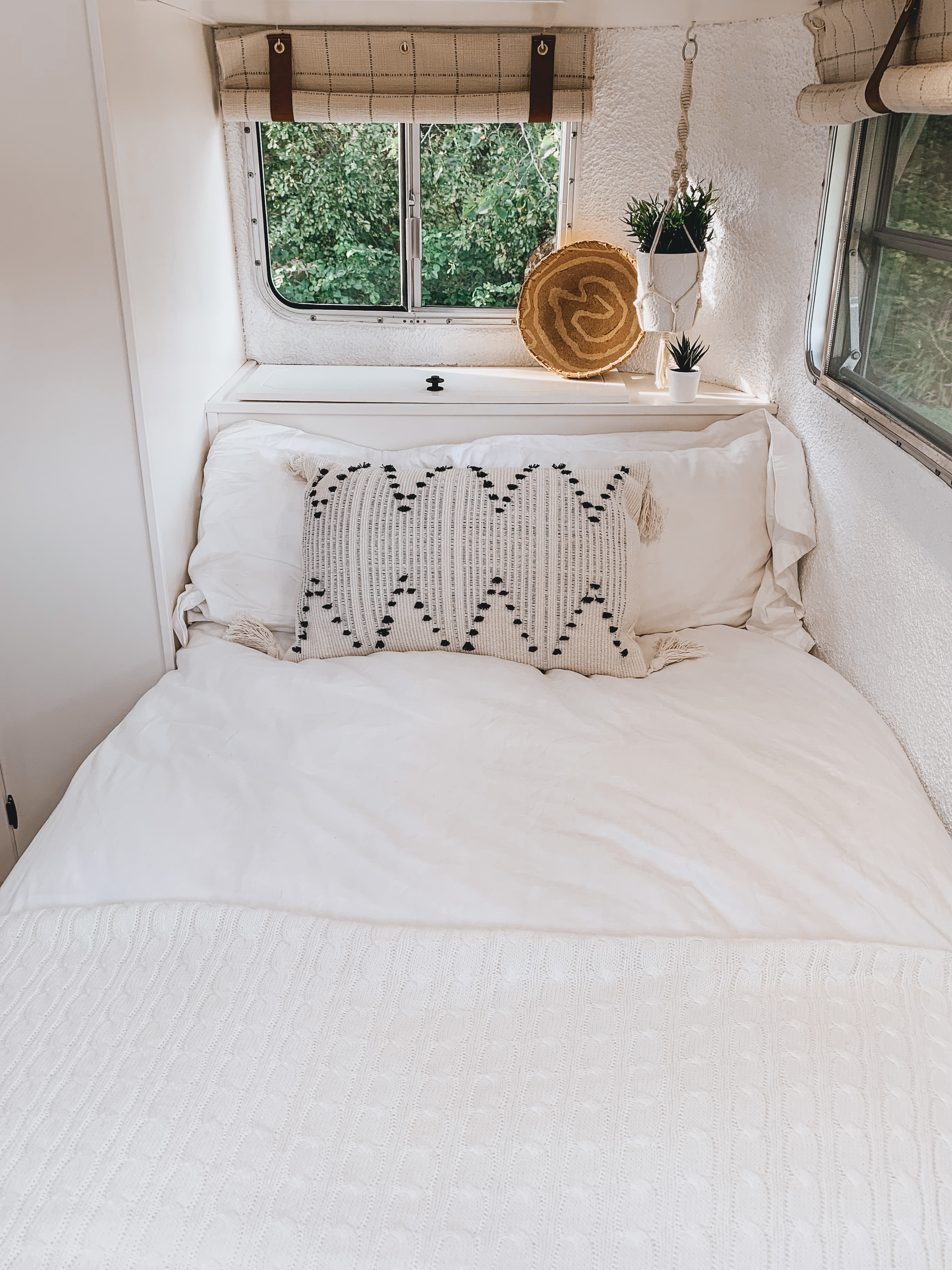 Explore a comfortable RV rental: white bedroom interior featuring a bed, decor, and window view of nature.. Vintage Trailers Boler 1978