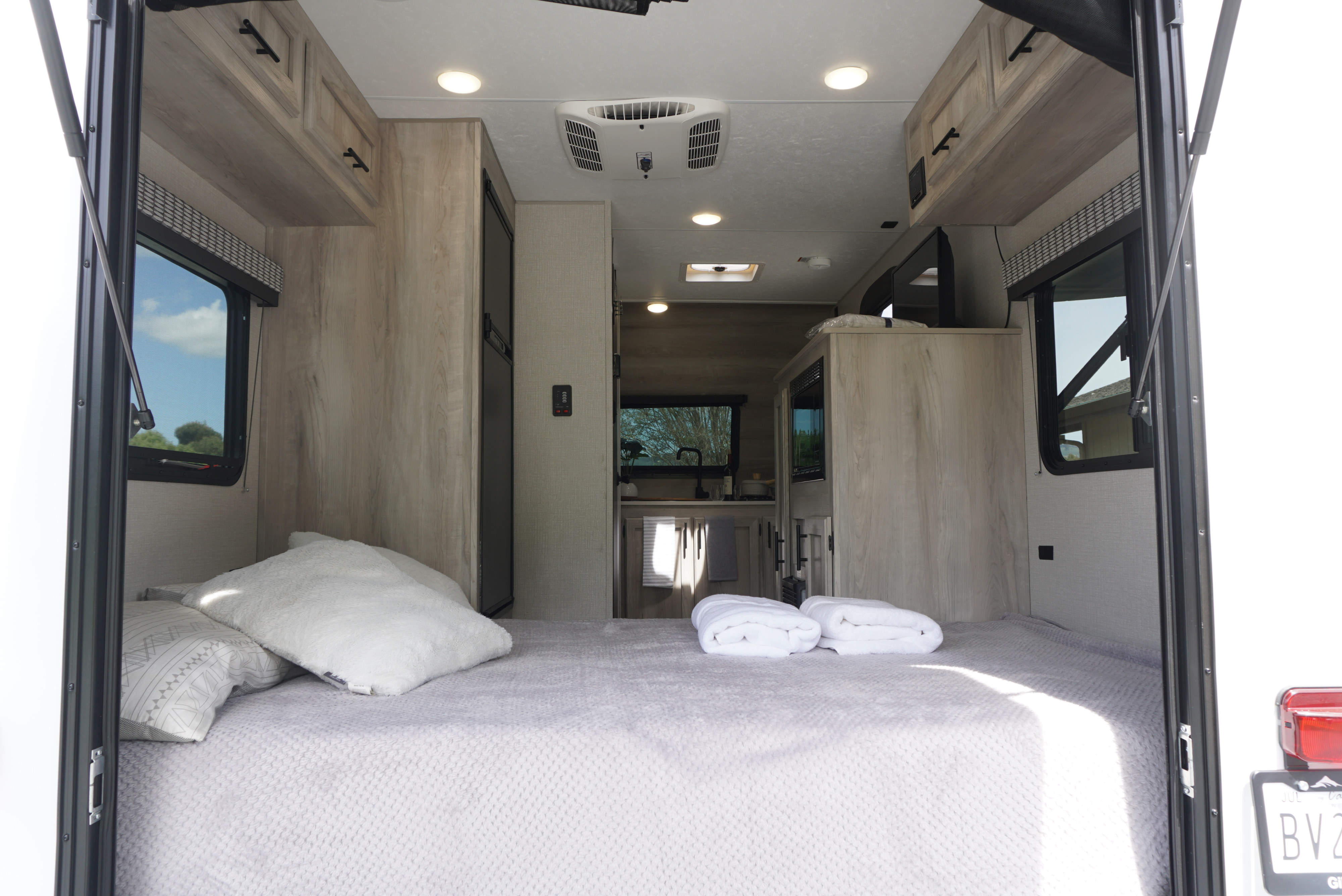 Inside an RV rental: A large, comfortable bed with light grey bedding dominates the foreground, leading to a modern kitchen.. KZ Escape Hatch 2021