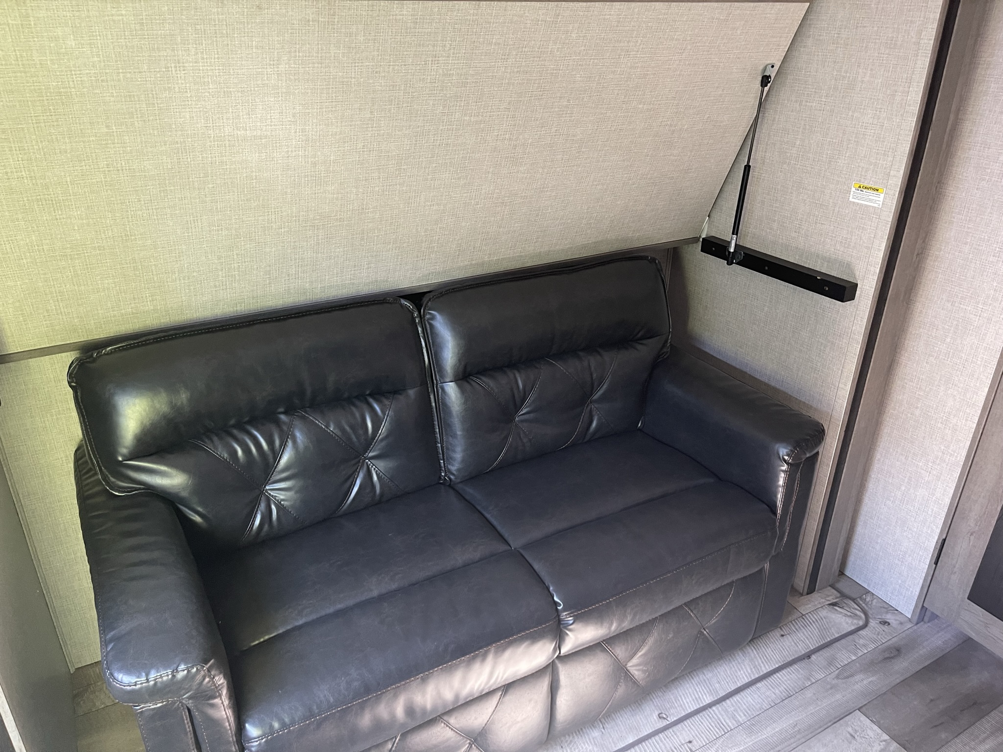 Black leather sofa in an RV rental, a compact two-seater with textured walls and wood-look flooring.. Keystone RV Outback 2021
