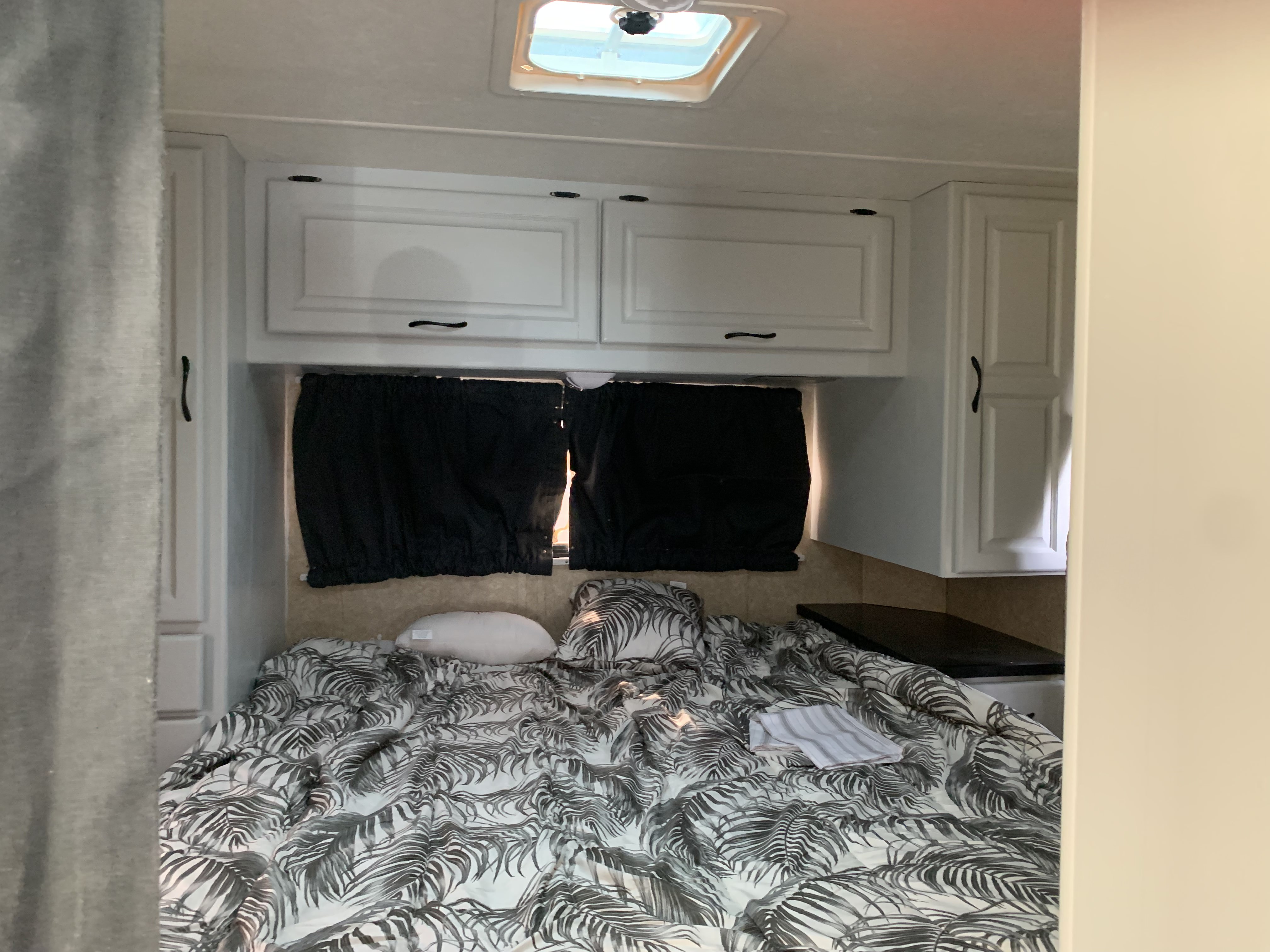 RV rental bedroom: bed with tropical palm-print bedding, white cabinets, and black window coverings.. Other Other 2008